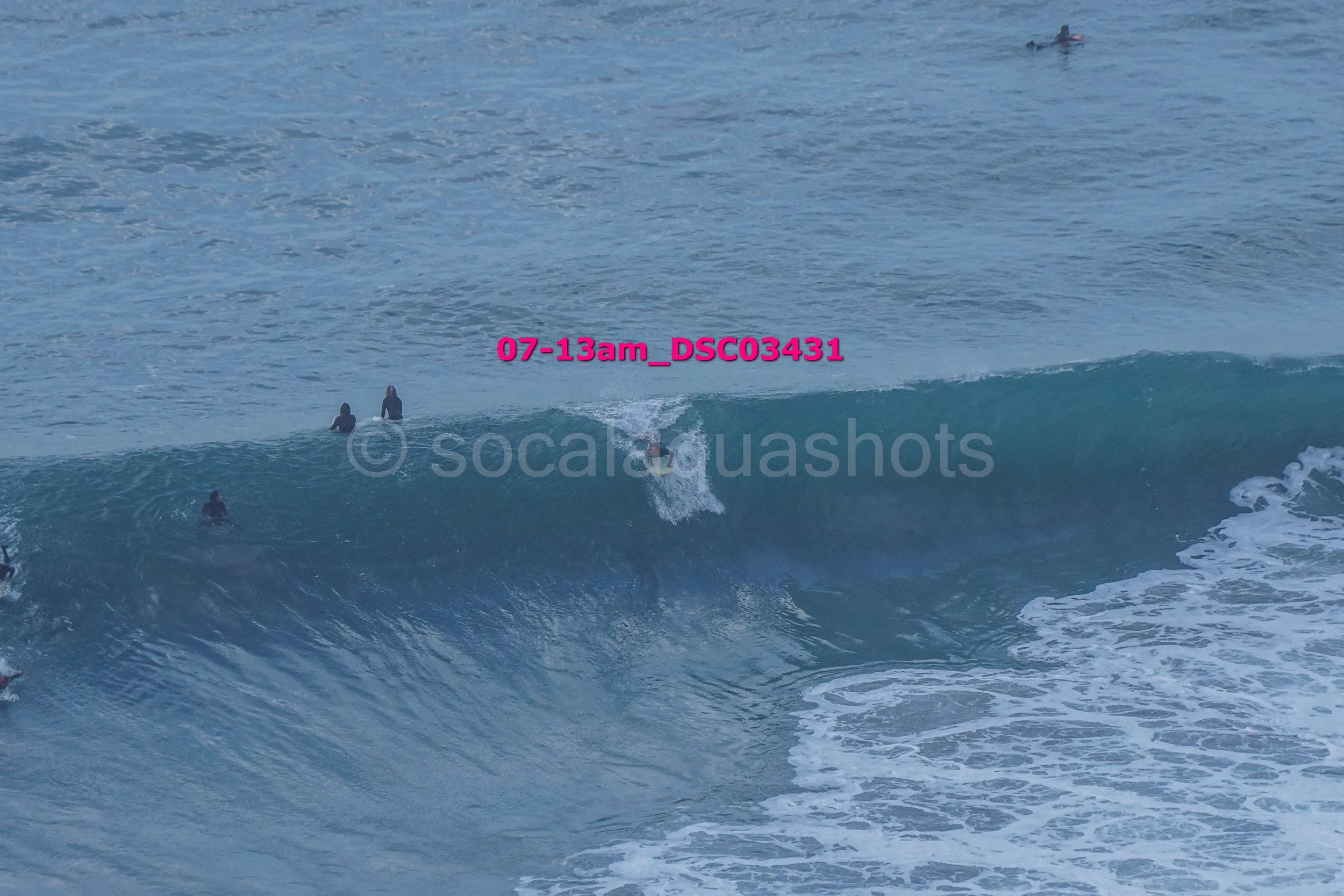 A person surfing on a large wave in the ocean with several other people in the water nearby.