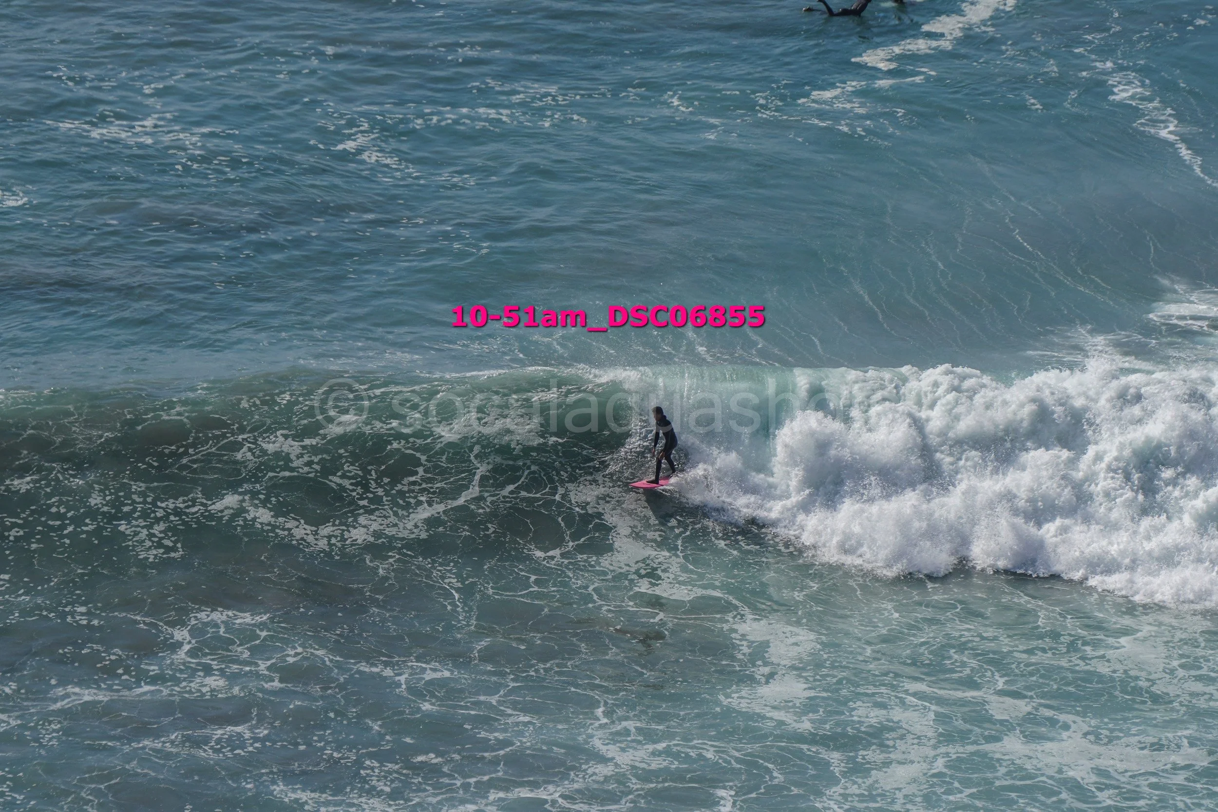 A person surfing on a pink surfboard on a wave in the ocean.