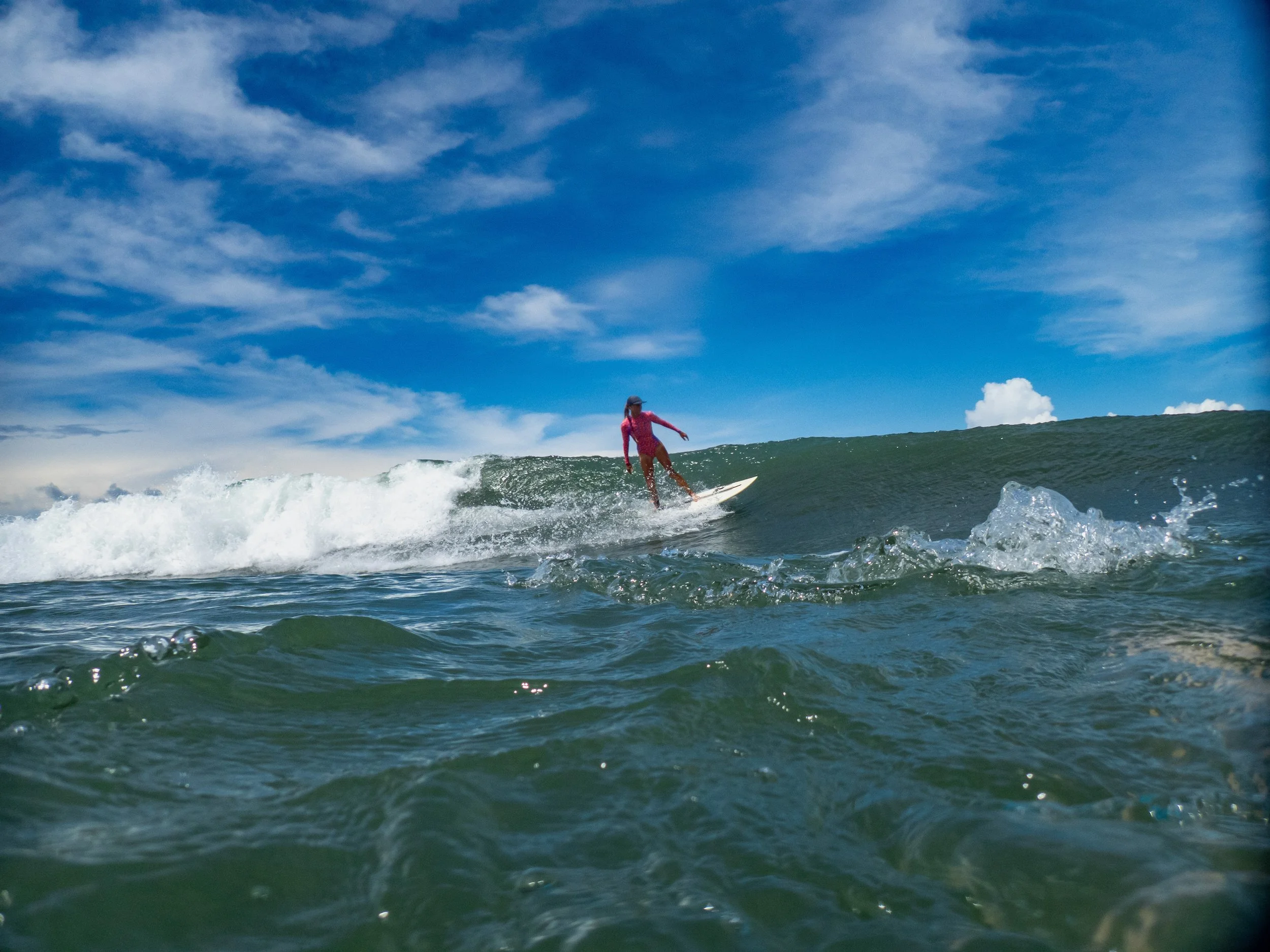A person surfing on a wave with a blue sky and some clouds in the background.