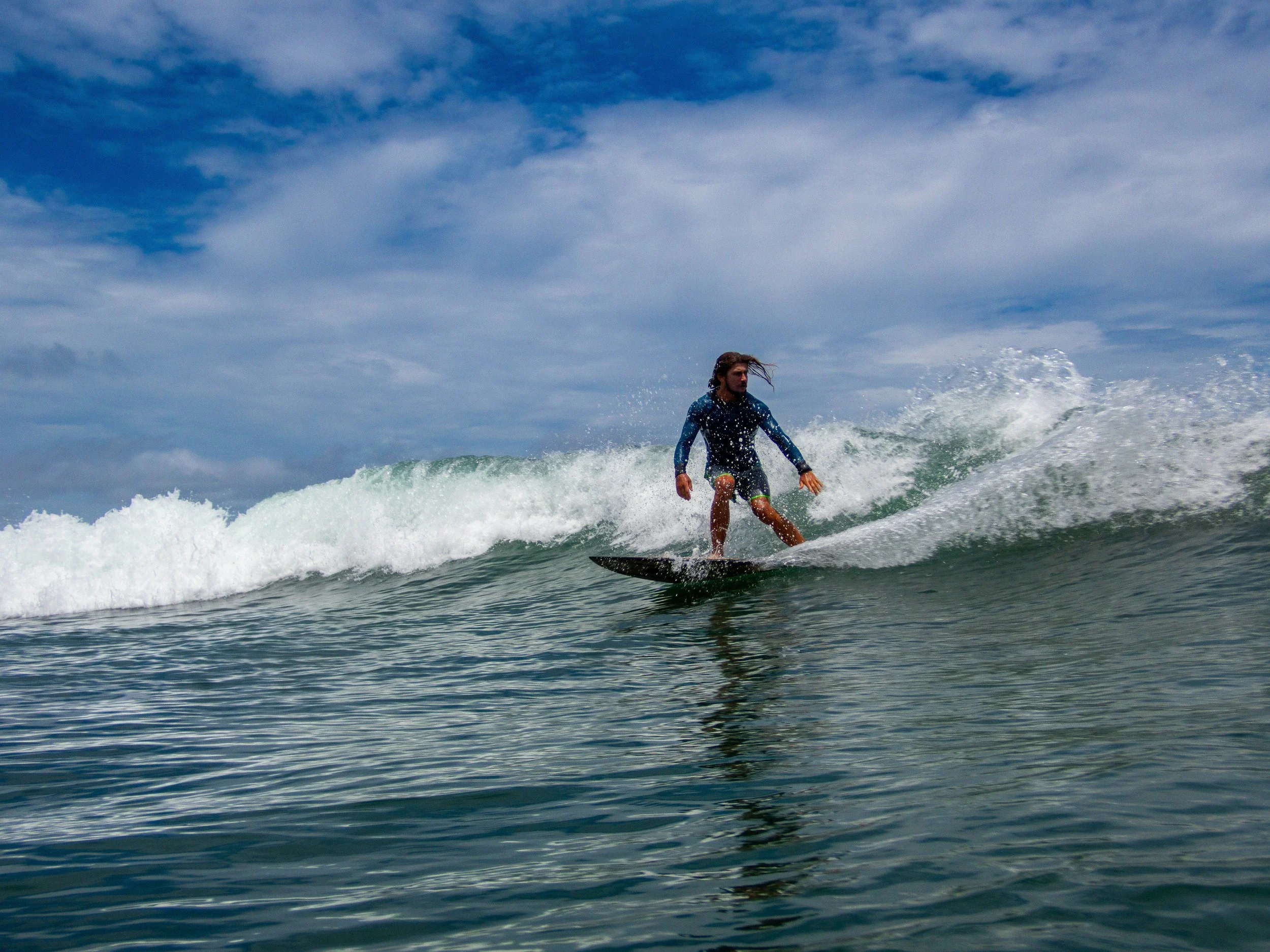 Surfer riding a wave in the ocean under a cloudy sky