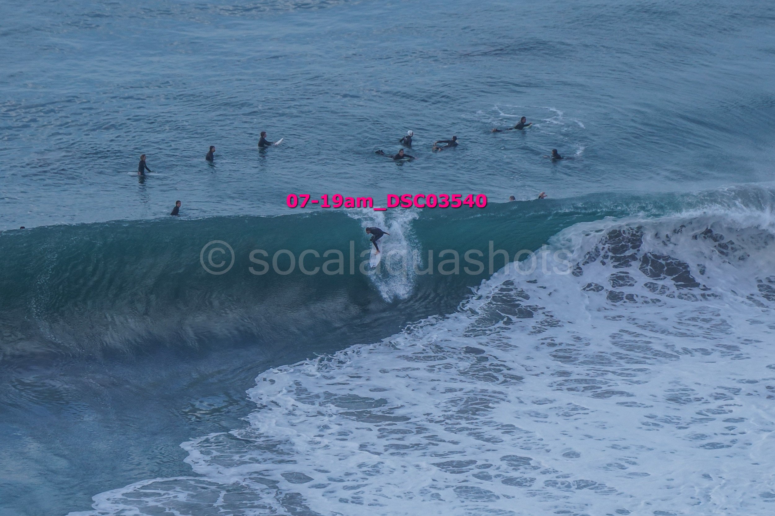 A person surfing a wave while other surfers wait in the water in the background.