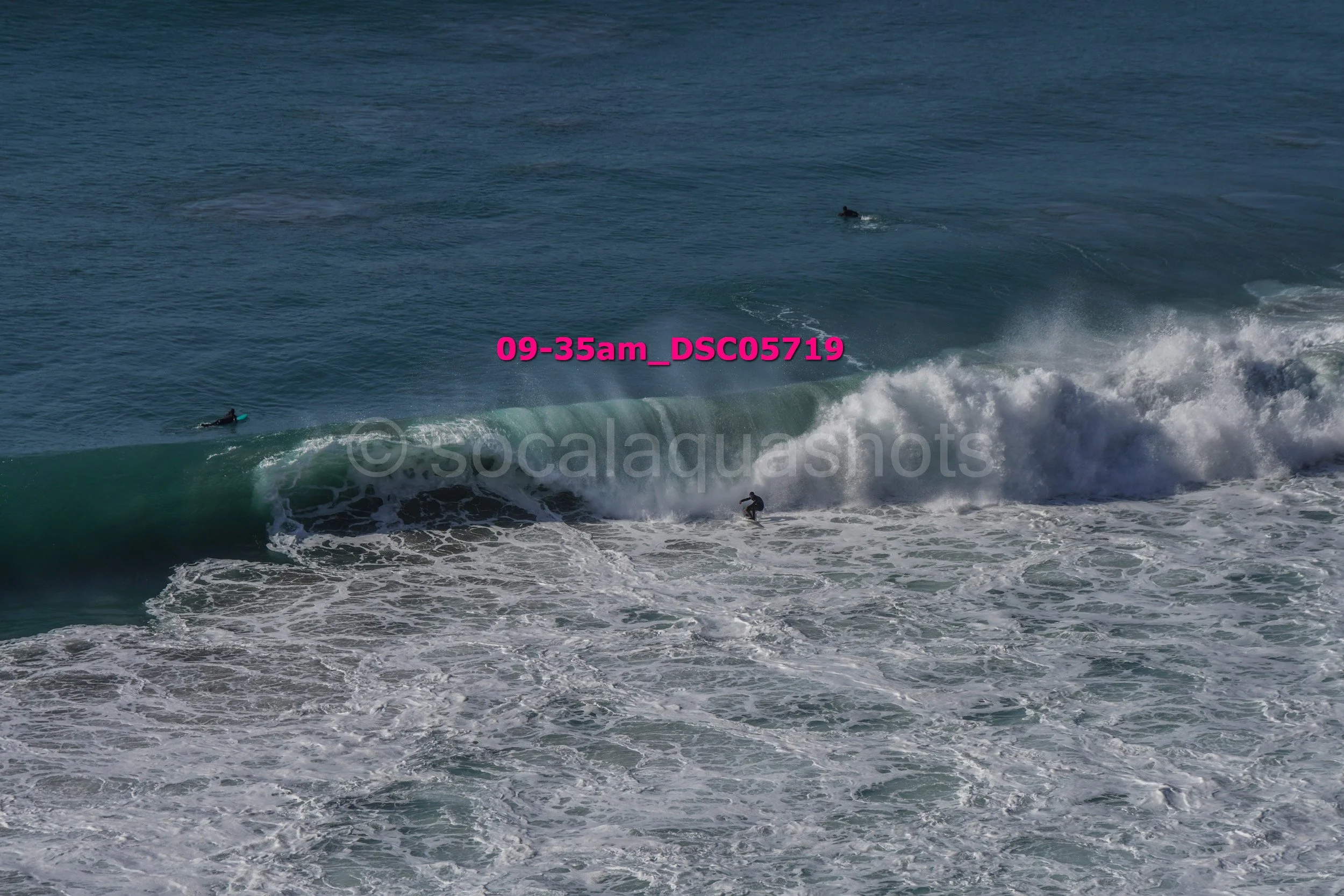 Several surfers riding a large ocean wave with some surfers in the water waiting for waves.