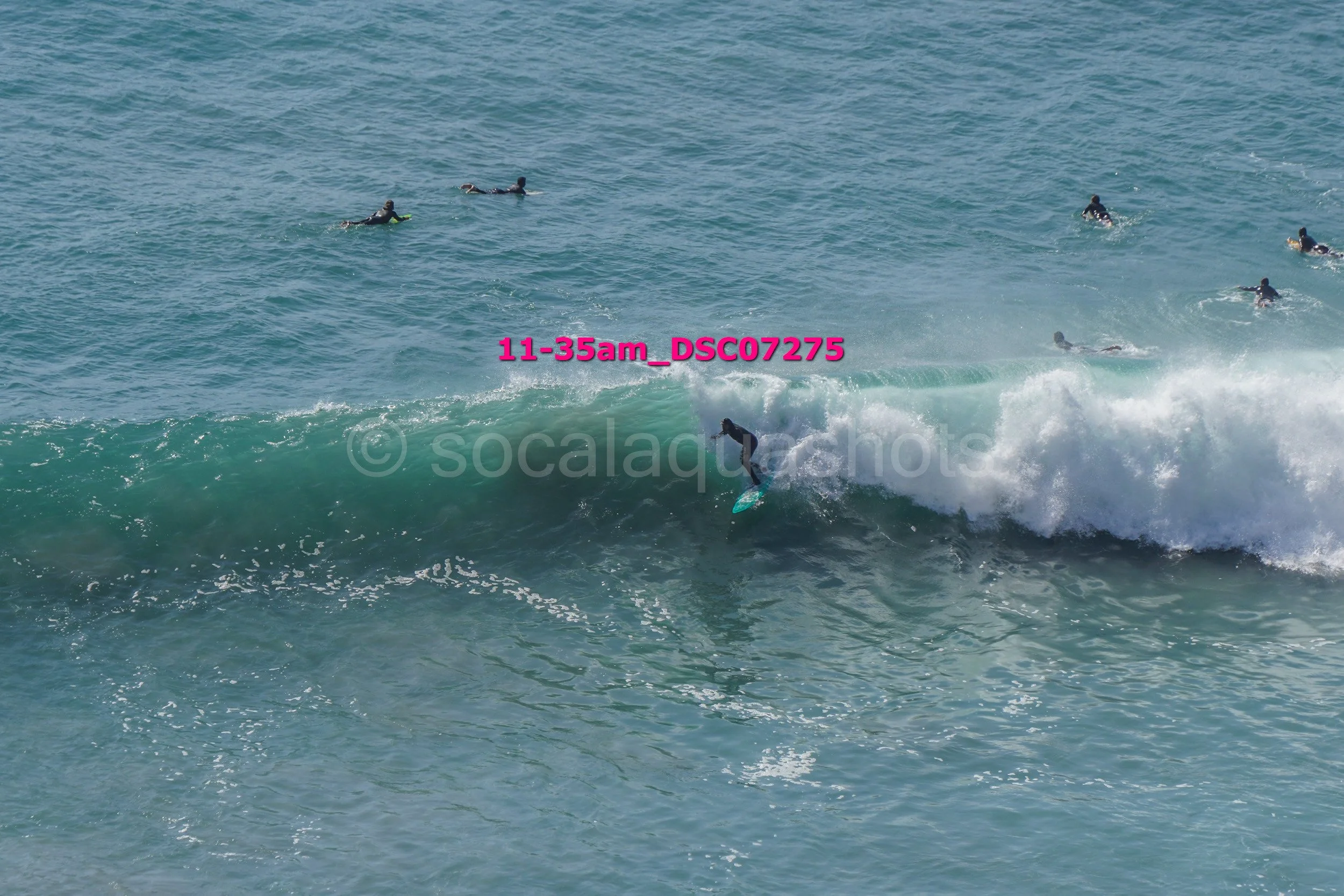 Surfer riding a wave with several people swimming in the ocean in the background.
