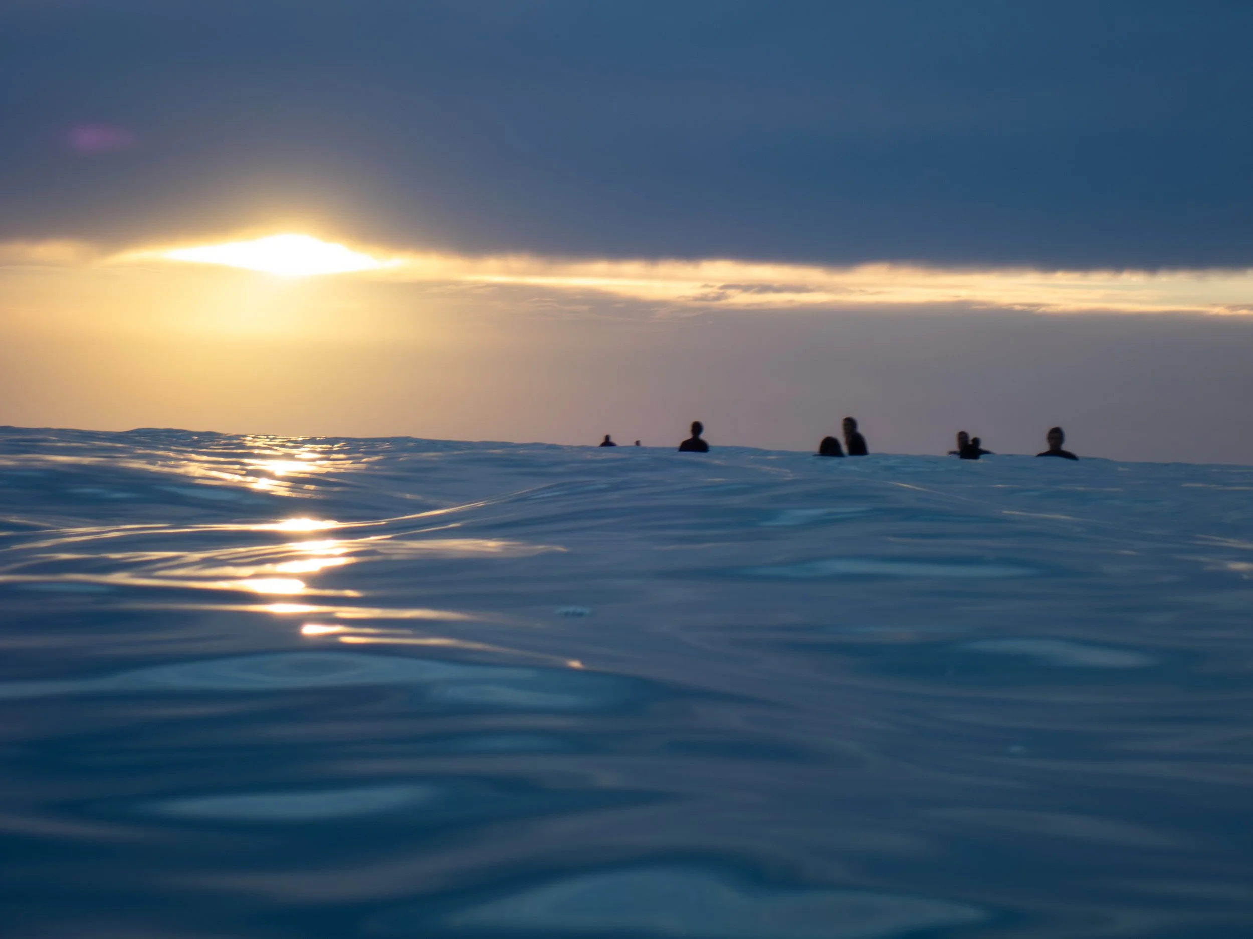 People swimming in the ocean during sunset or sunrise with a cloudy sky overhead.