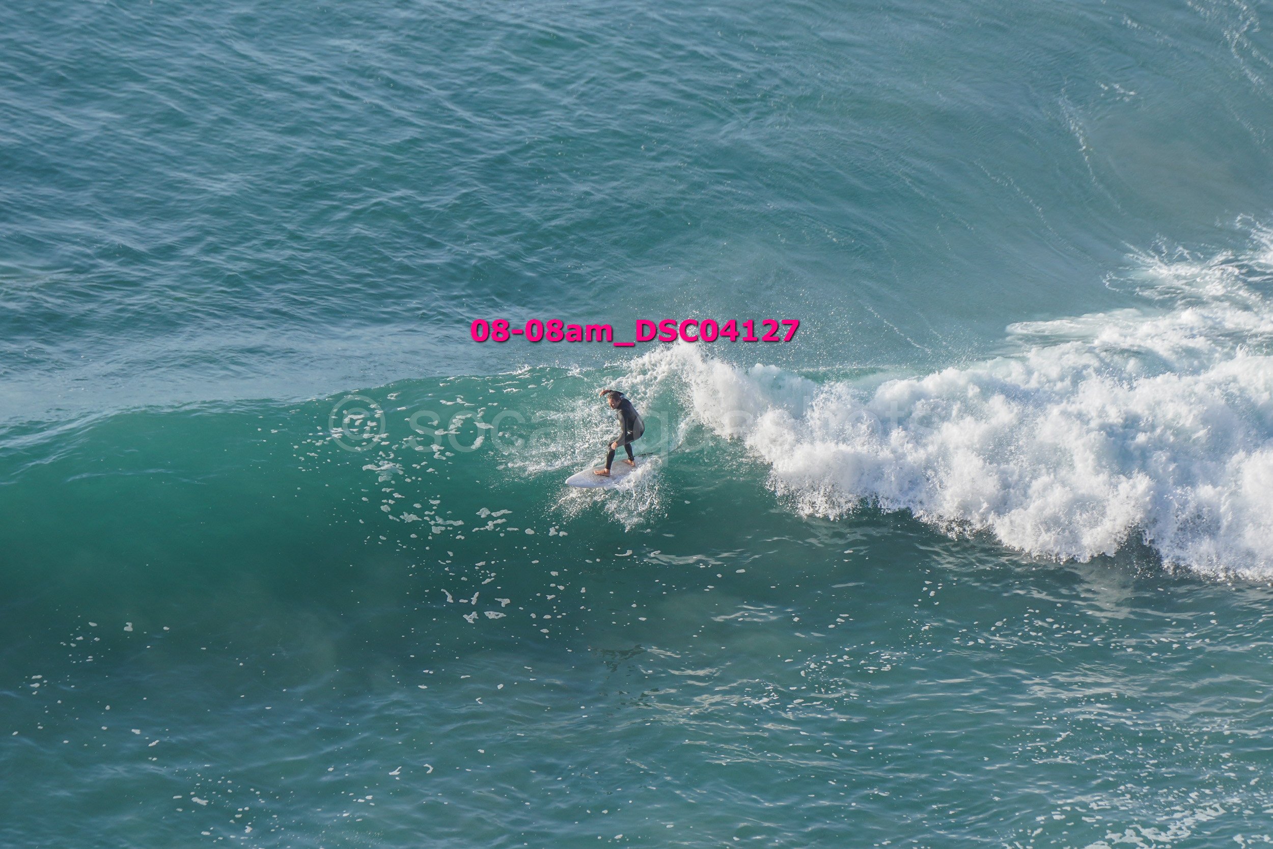 A person surfing on a wave in the ocean, wearing a black wetsuit.