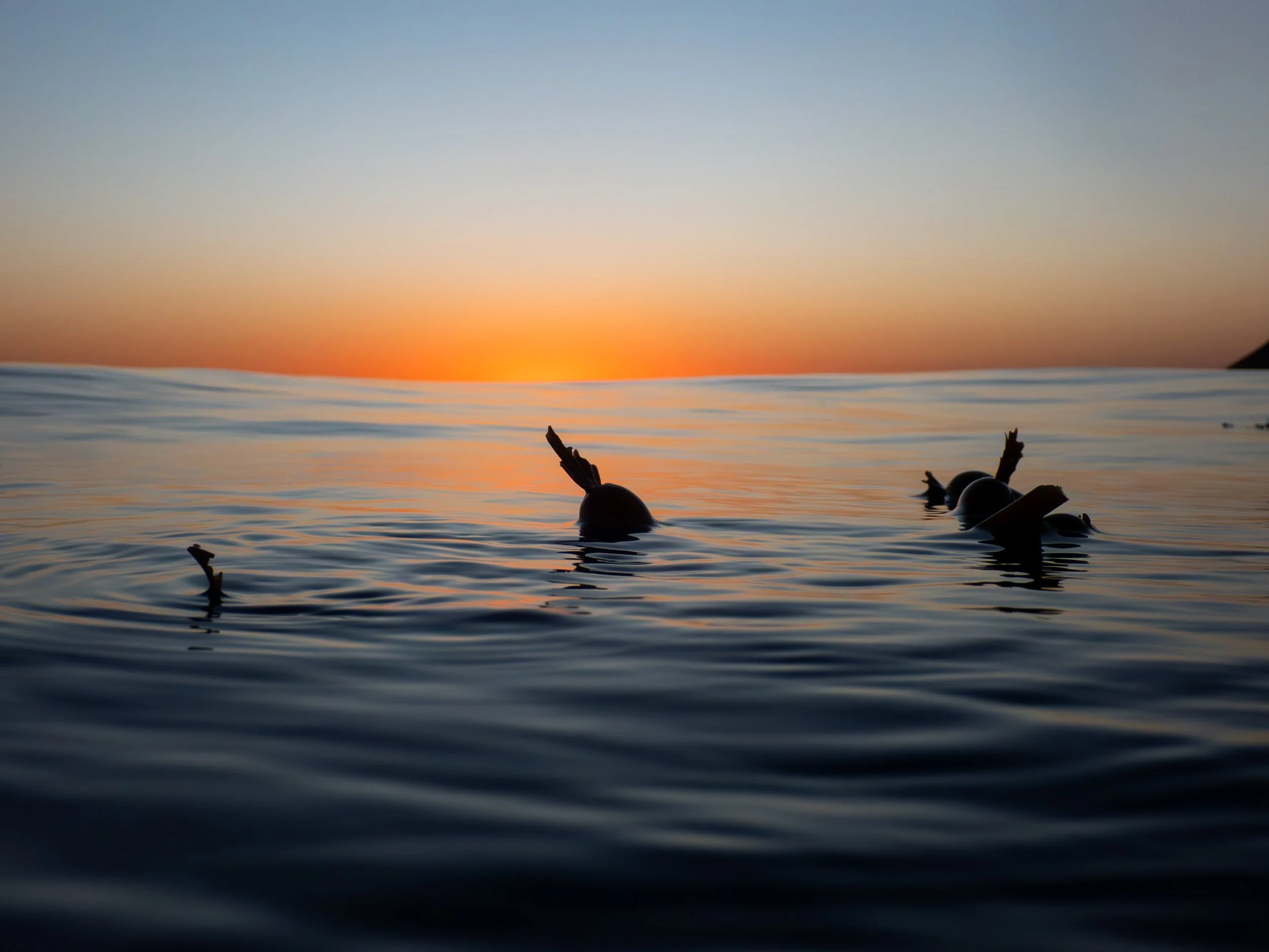 Lighthouse on the horizon during sunset with small boats floating in the water in the foreground.
