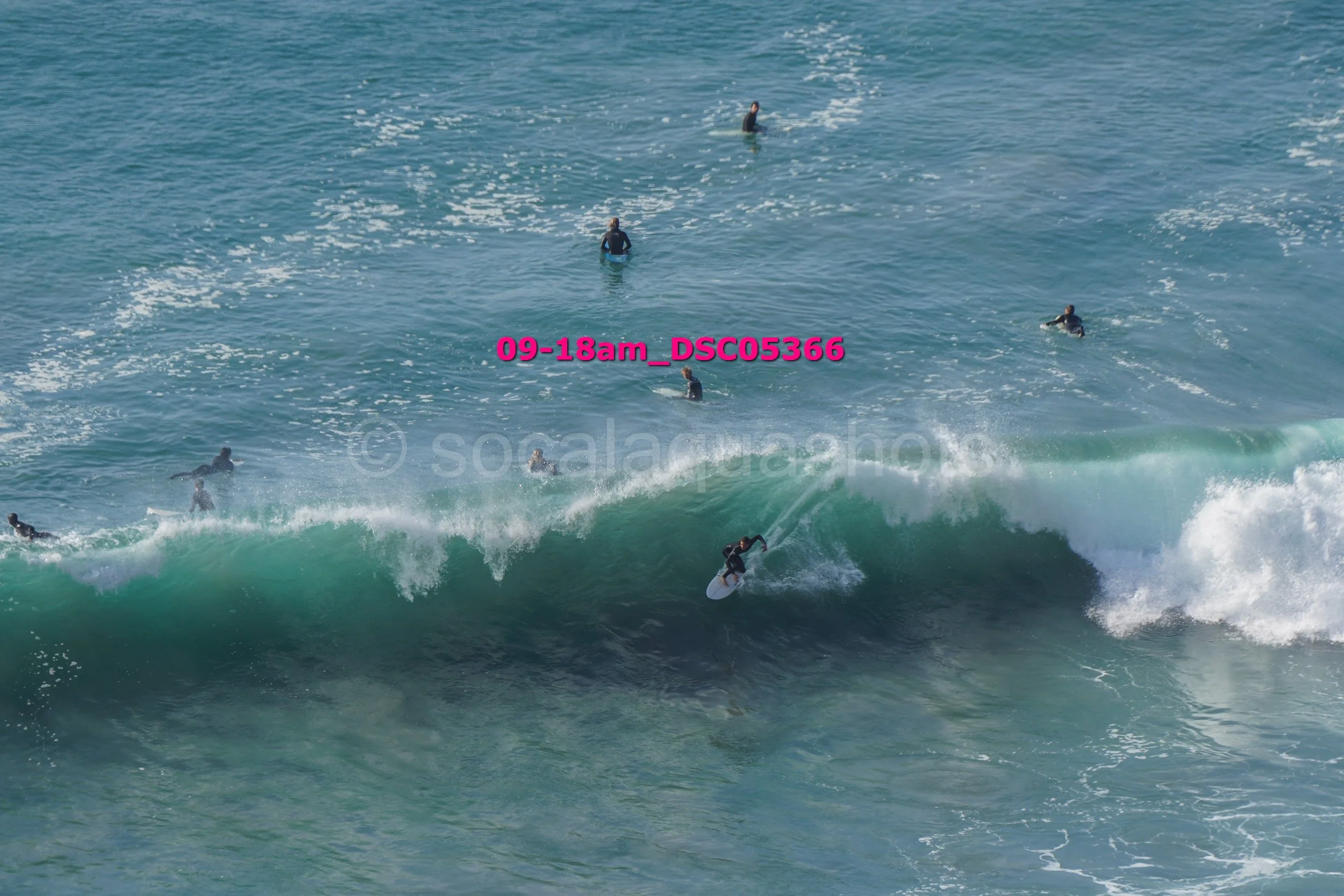 A person surfing a large wave while several others are swimming or surfing in the ocean behind.