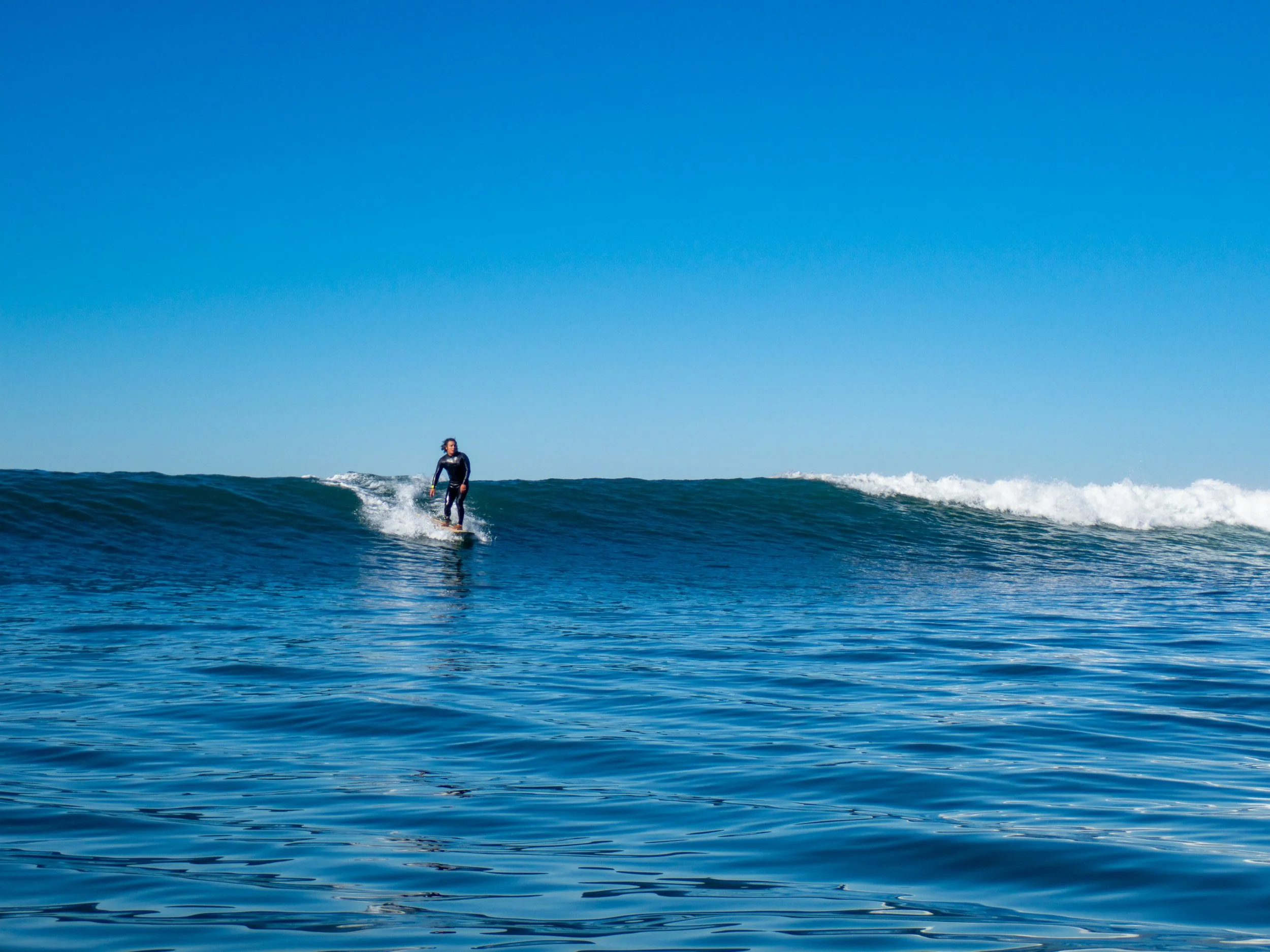 A person surfing on a wave in the ocean during the daytime under a clear blue sky.