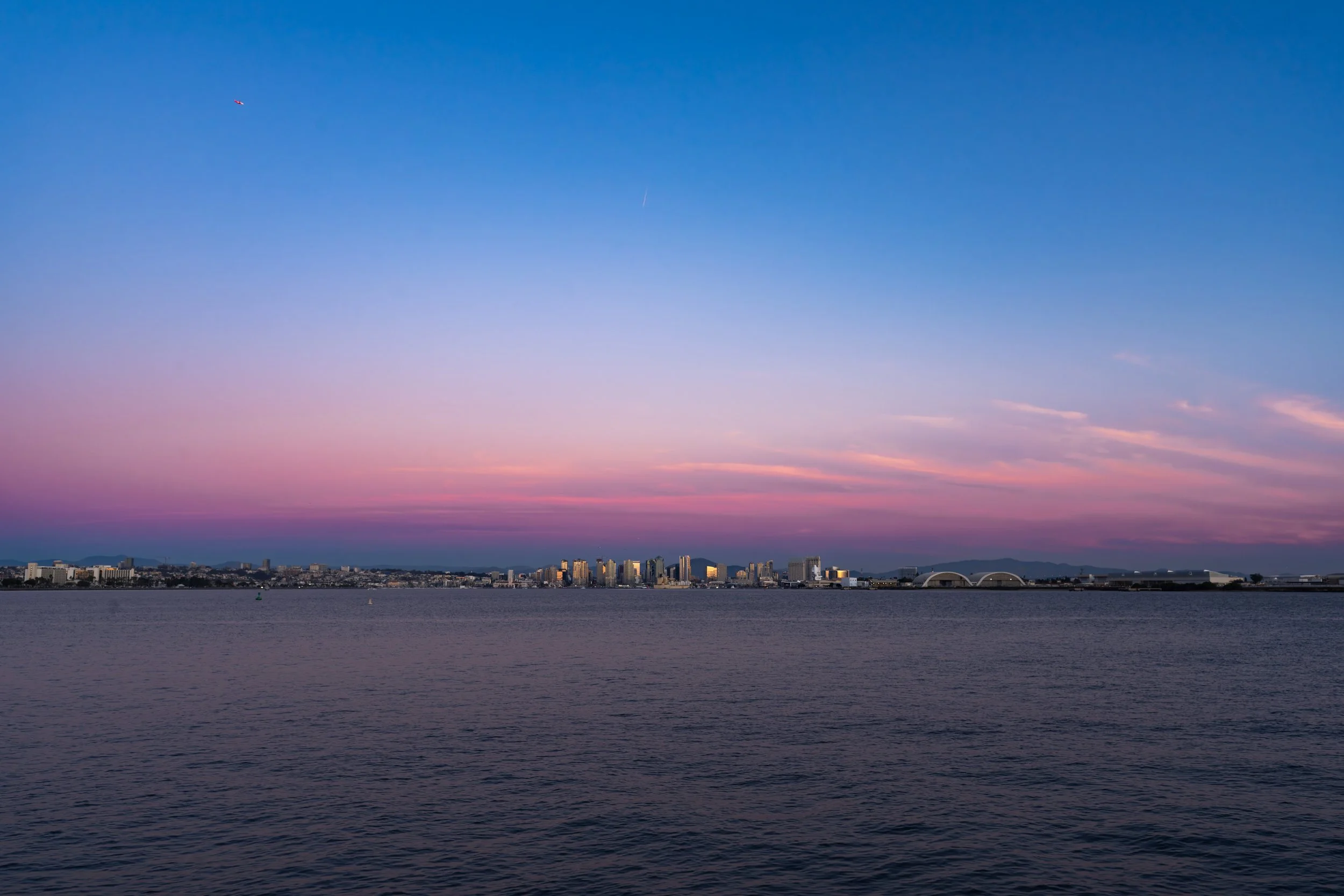 A city skyline across a body of water during sunset with a sky transitioning from blue to pink and purple hues.