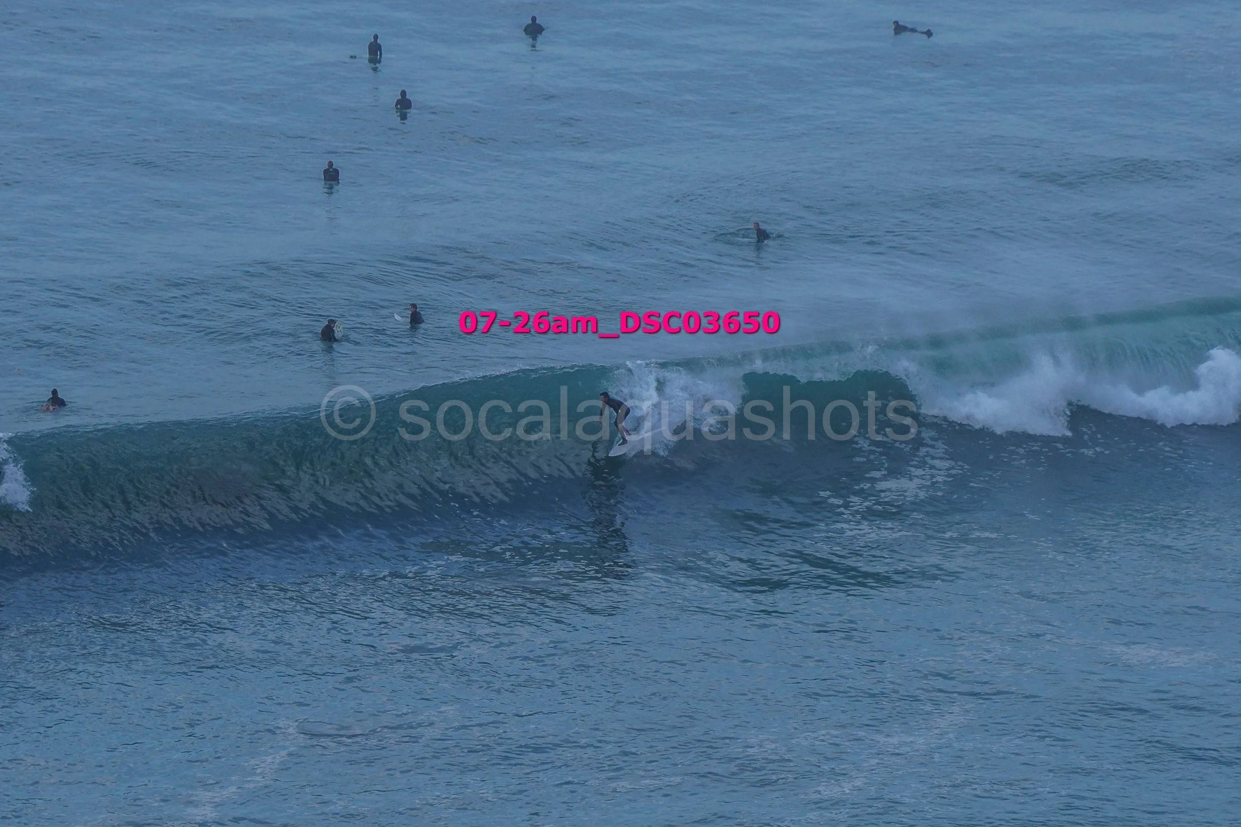 Surfer riding a wave at the beach with several people swimming in the water in the background.
