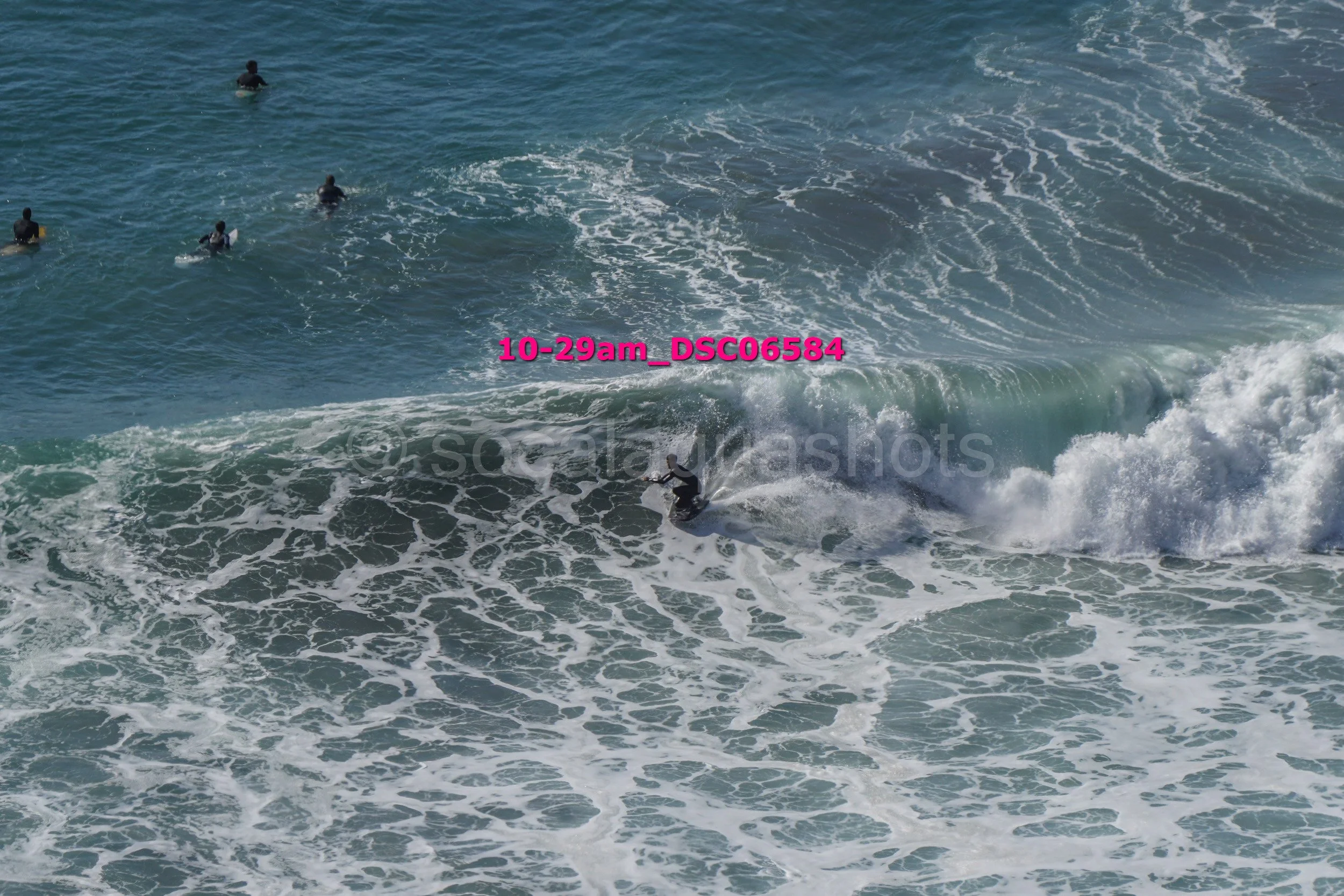Surfer riding a wave in the ocean with other surfers floating nearby