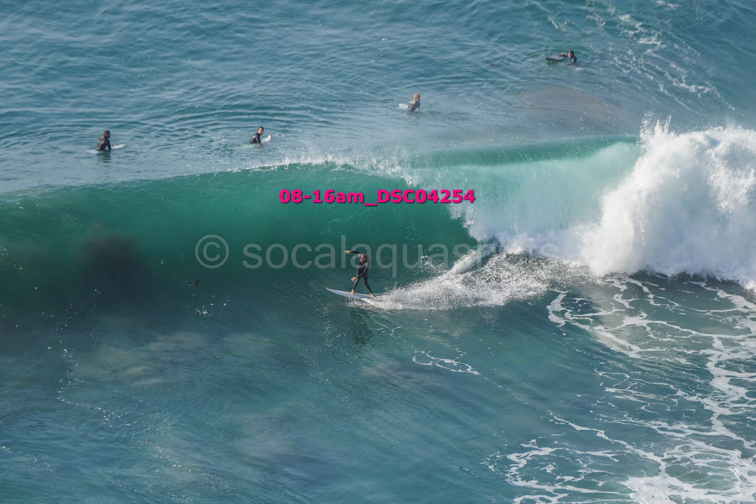 Surfer riding a large wave with several surfers in the water in the background.