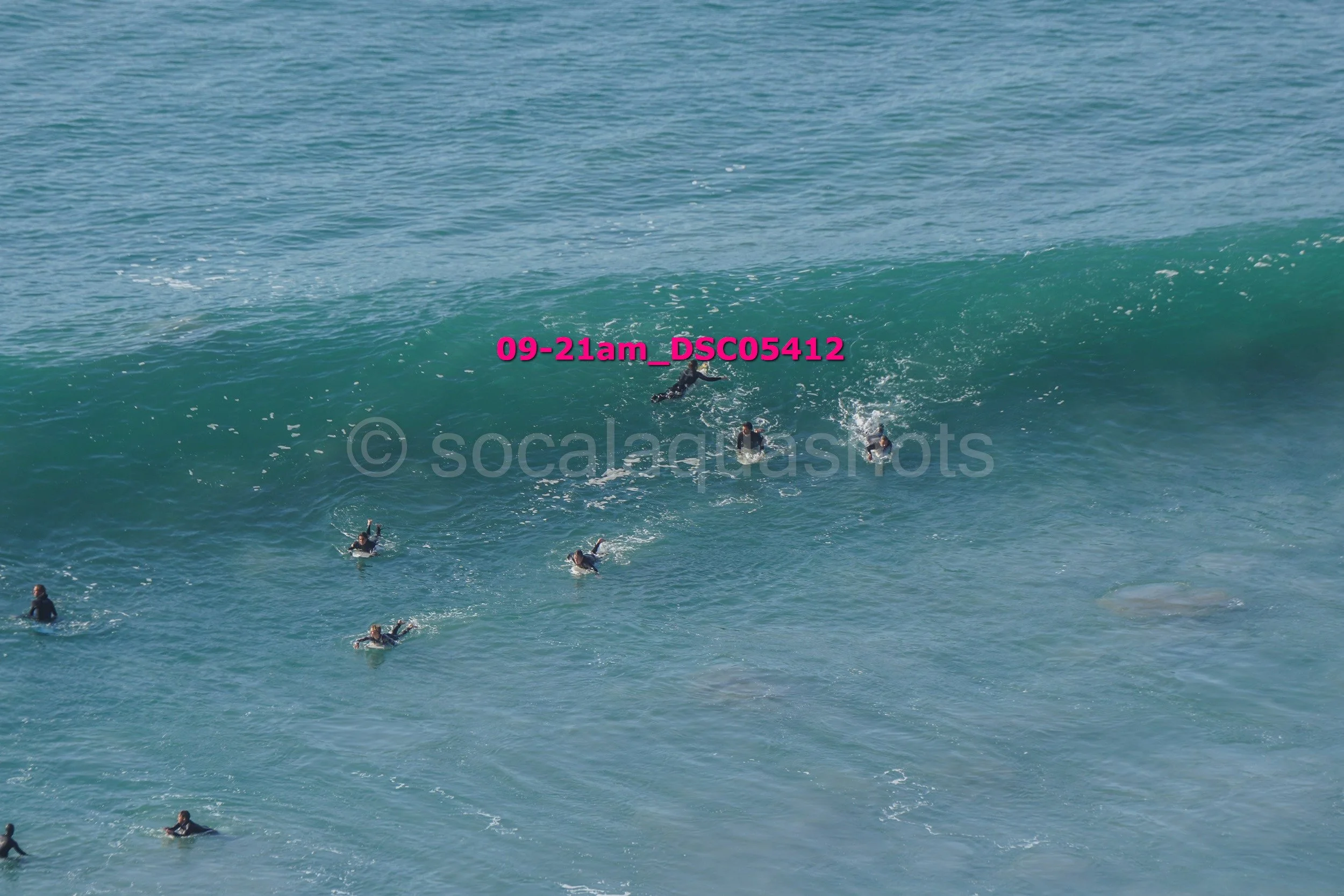 Surfers riding a large ocean wave with some surfers waiting in the water.