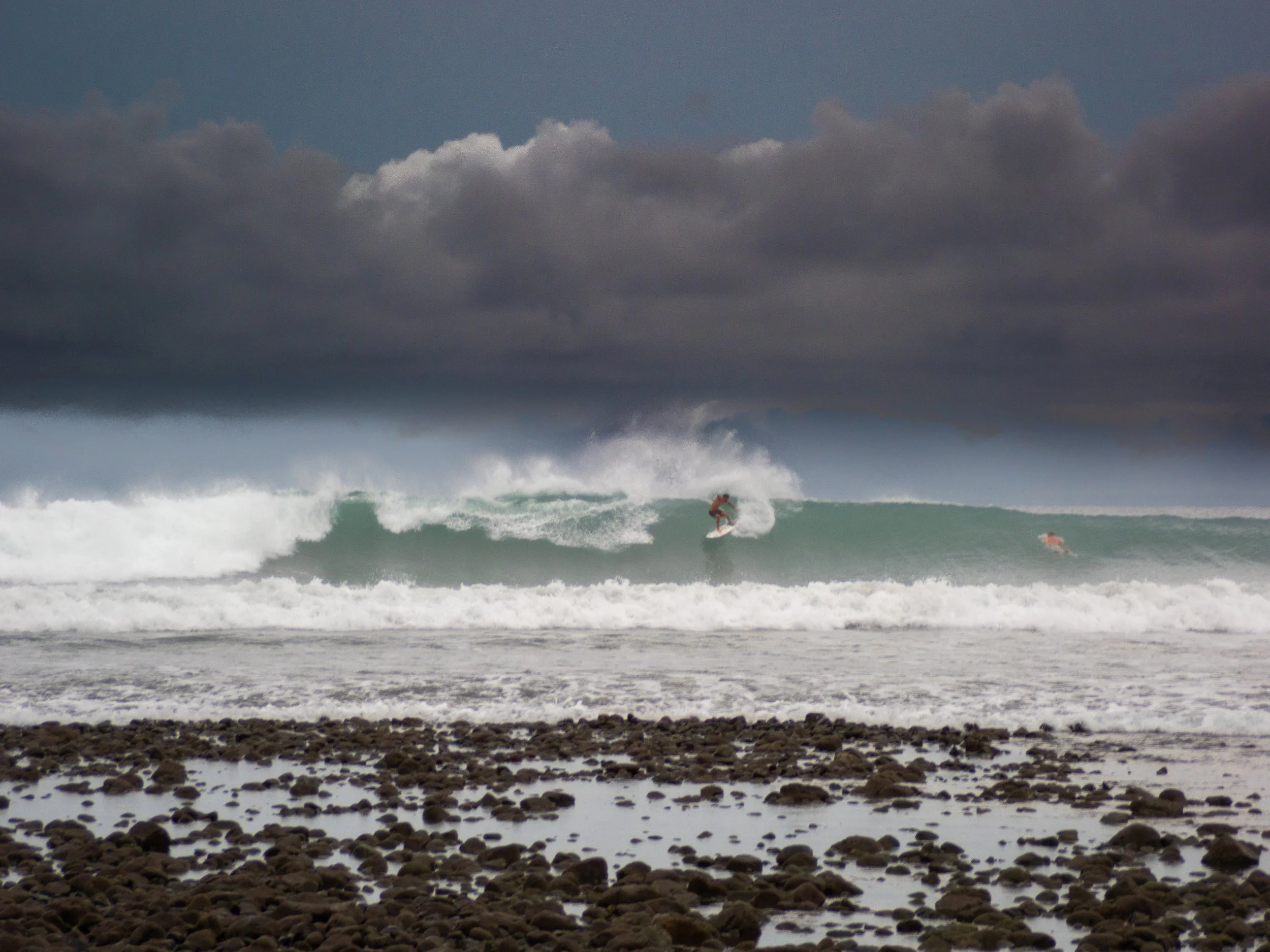 Surfer riding a wave near rocky shore under cloudy sky