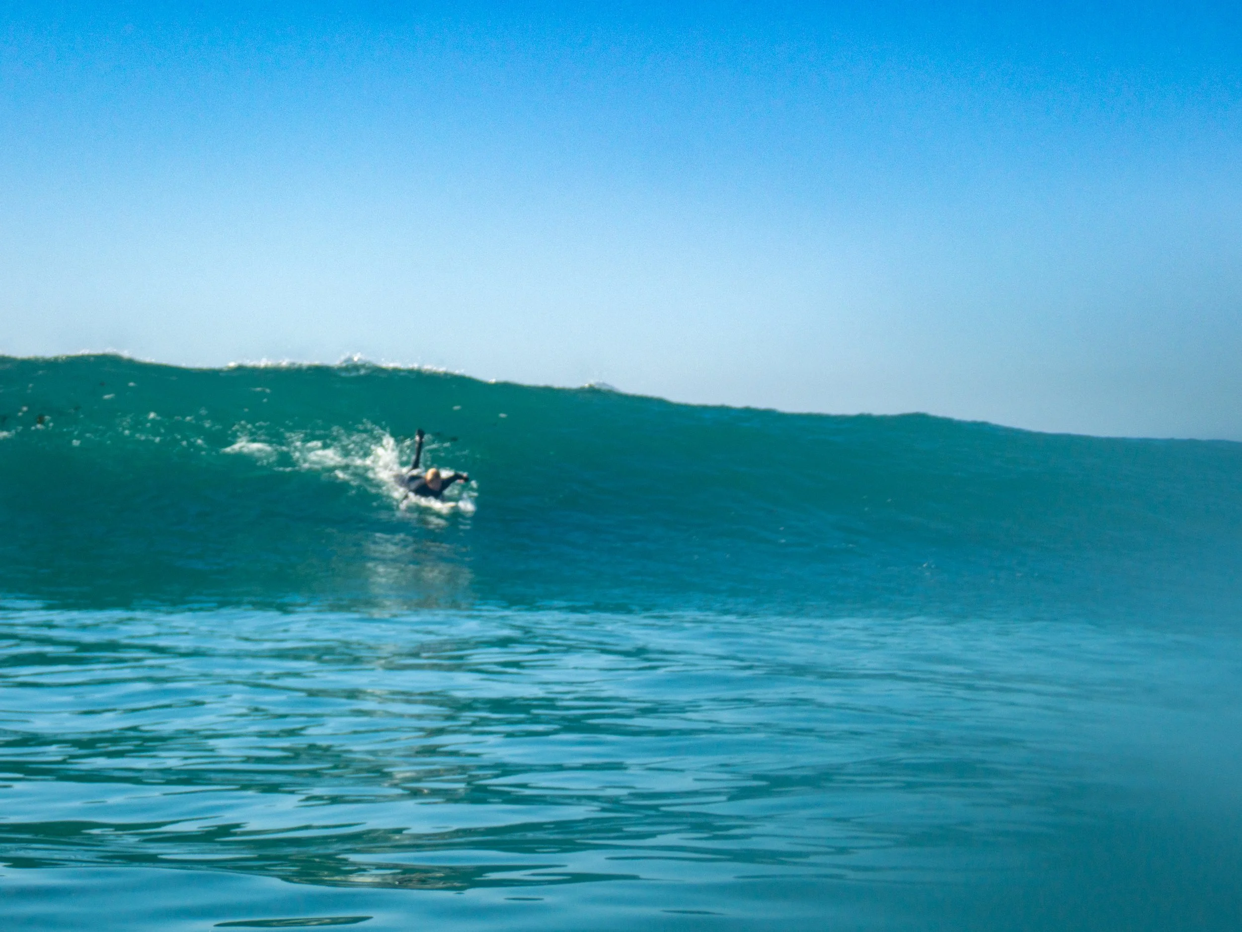 Surfer riding a large wave in the ocean on a clear day with blue sky.