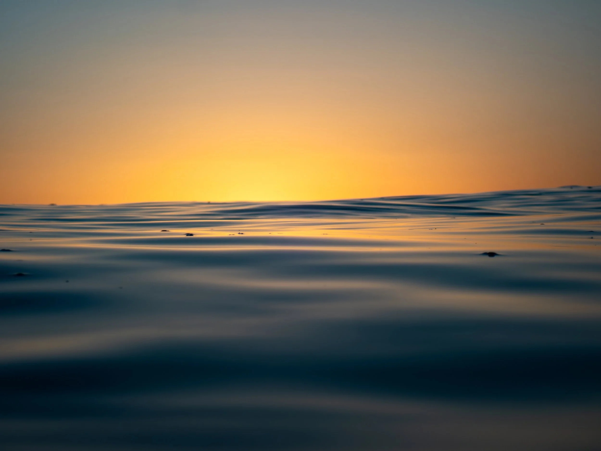 A calm ocean at sunset with a clear horizon and a gradient sky transitioning from blue to orange.