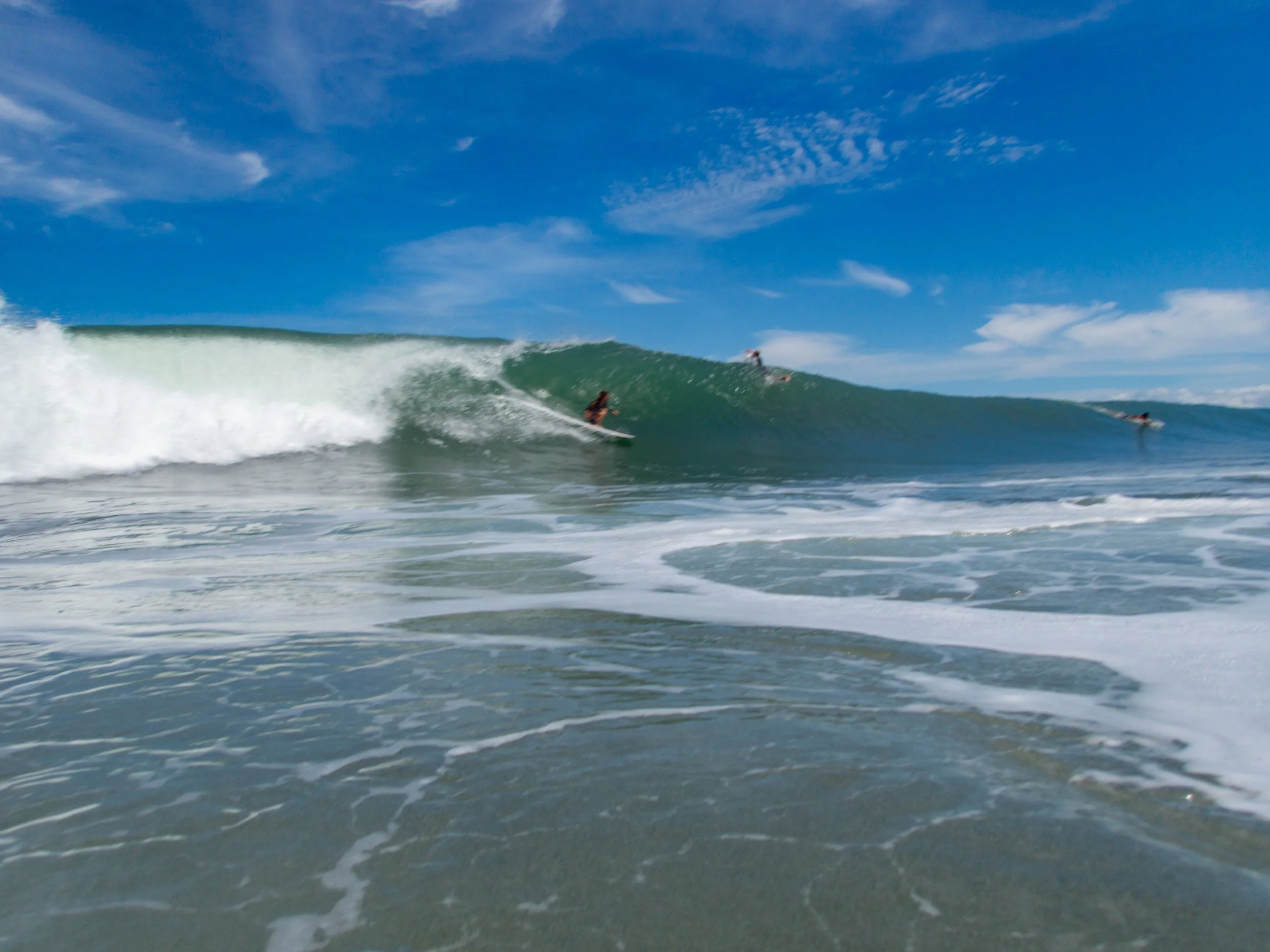 Surfer riding a large ocean wave under a clear blue sky