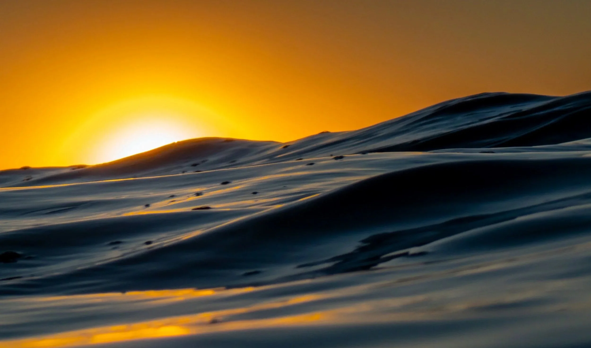 Sun setting over ocean waves with a yellow-orange sky in the background.