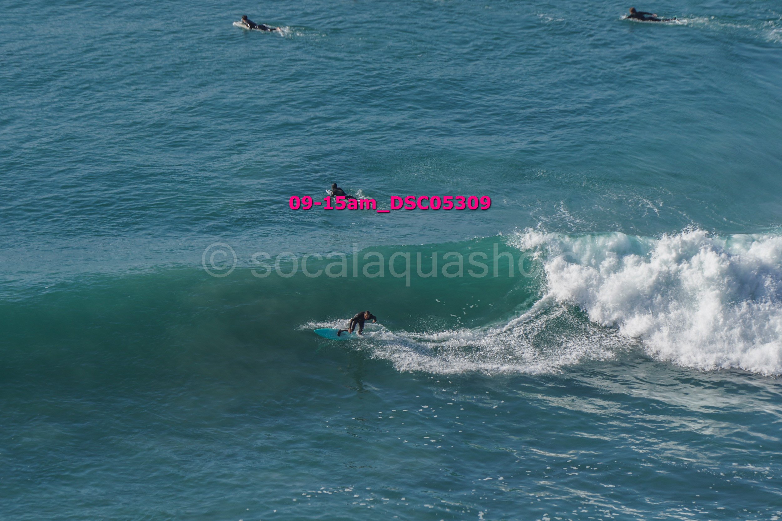 Surfer riding a wave with other surfers in the distance, ocean in the background.