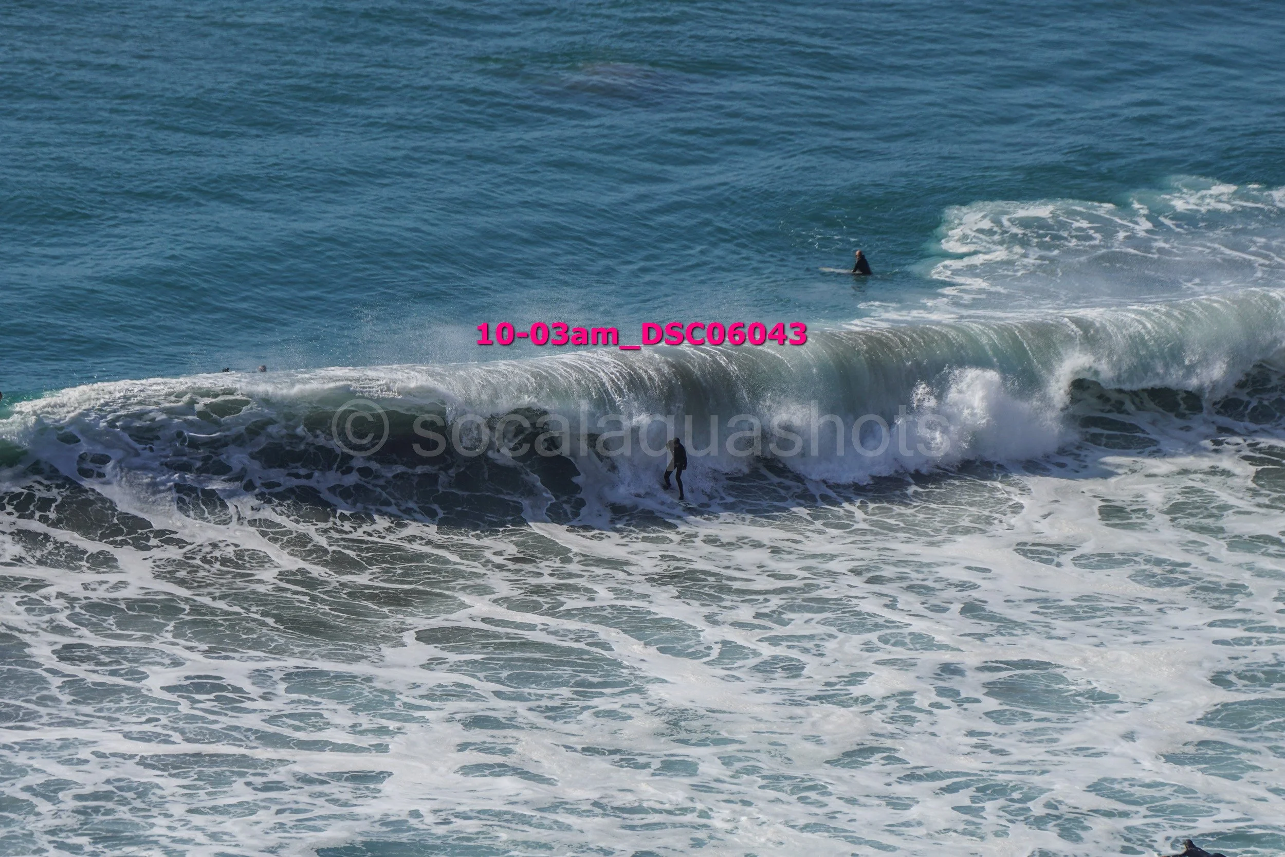 A person surfing on a wave in the ocean, with another person swimming in the background.