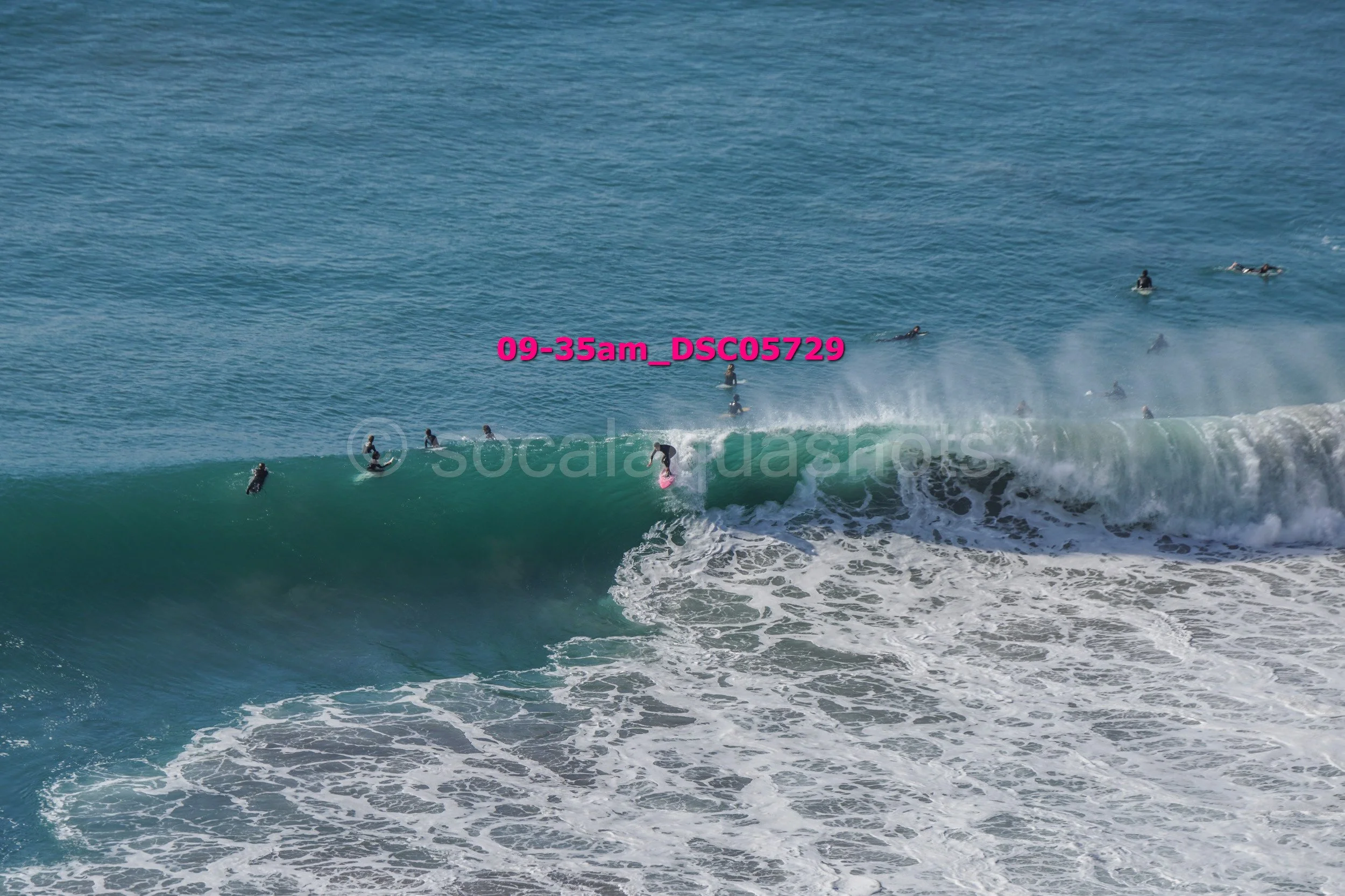 Surfers in the ocean waiting for waves, with one surfer riding a wave near the center of the image.