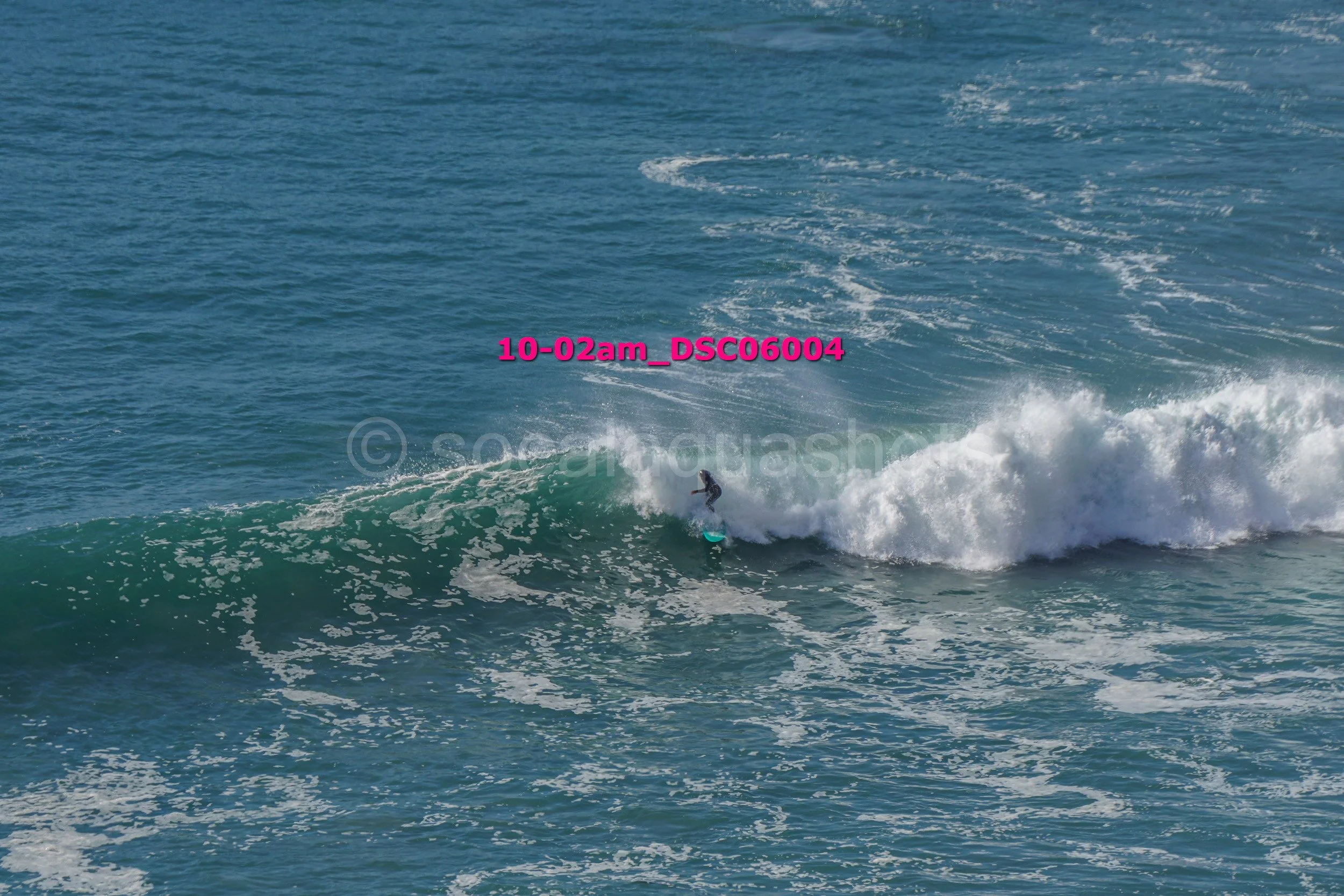 A person surfing on a small wave in the ocean with a clear blue sky in the background.