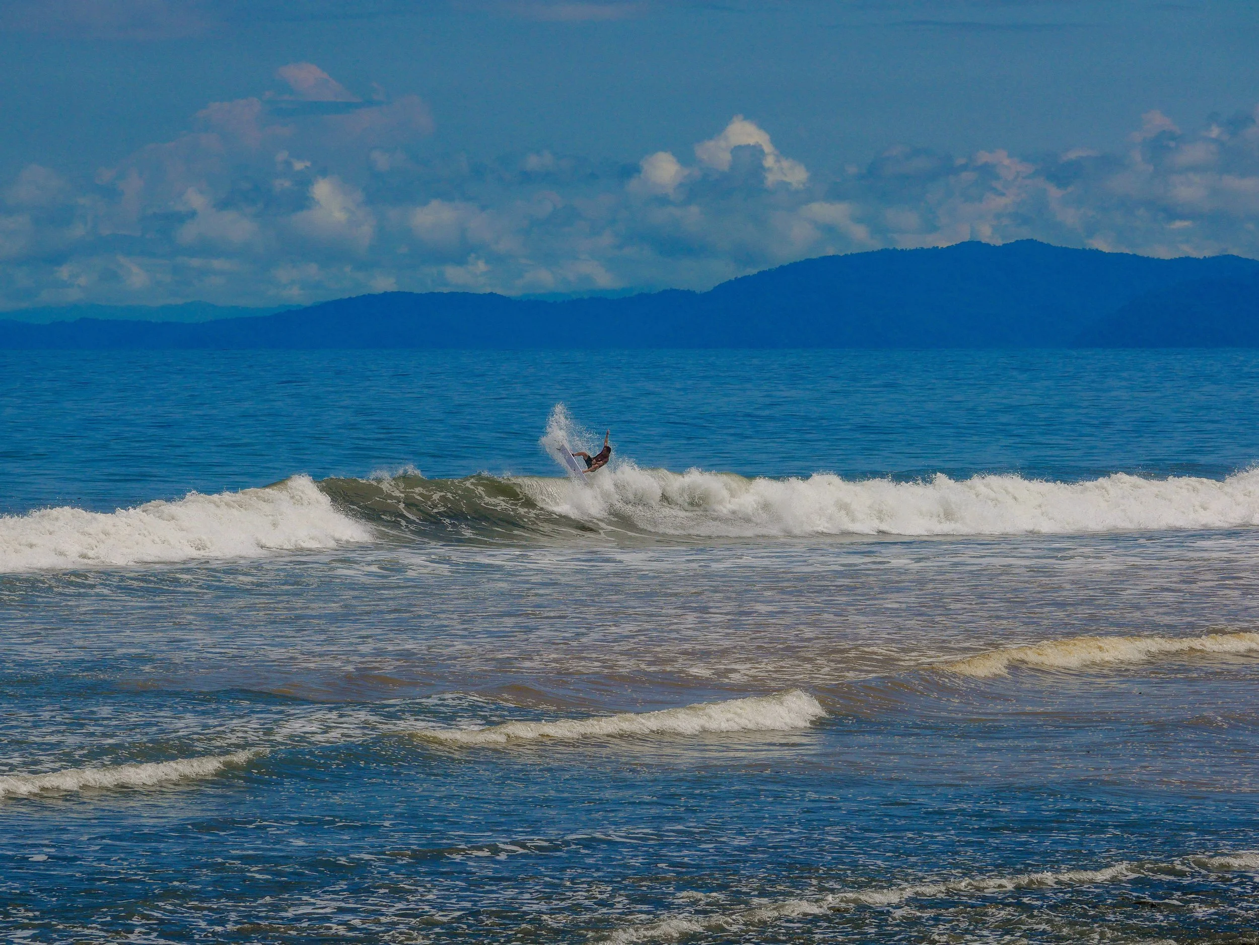 Surfer riding a wave in an ocean with a mountainous backdrop