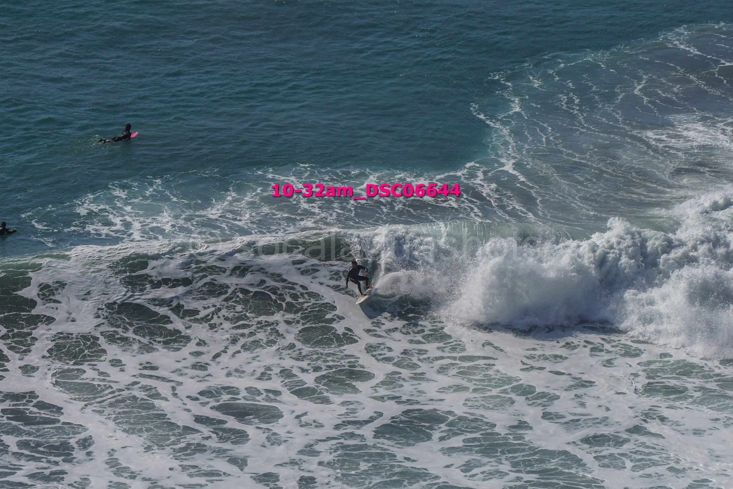Surfer riding a wave in the ocean with two other surfers in the water nearby.