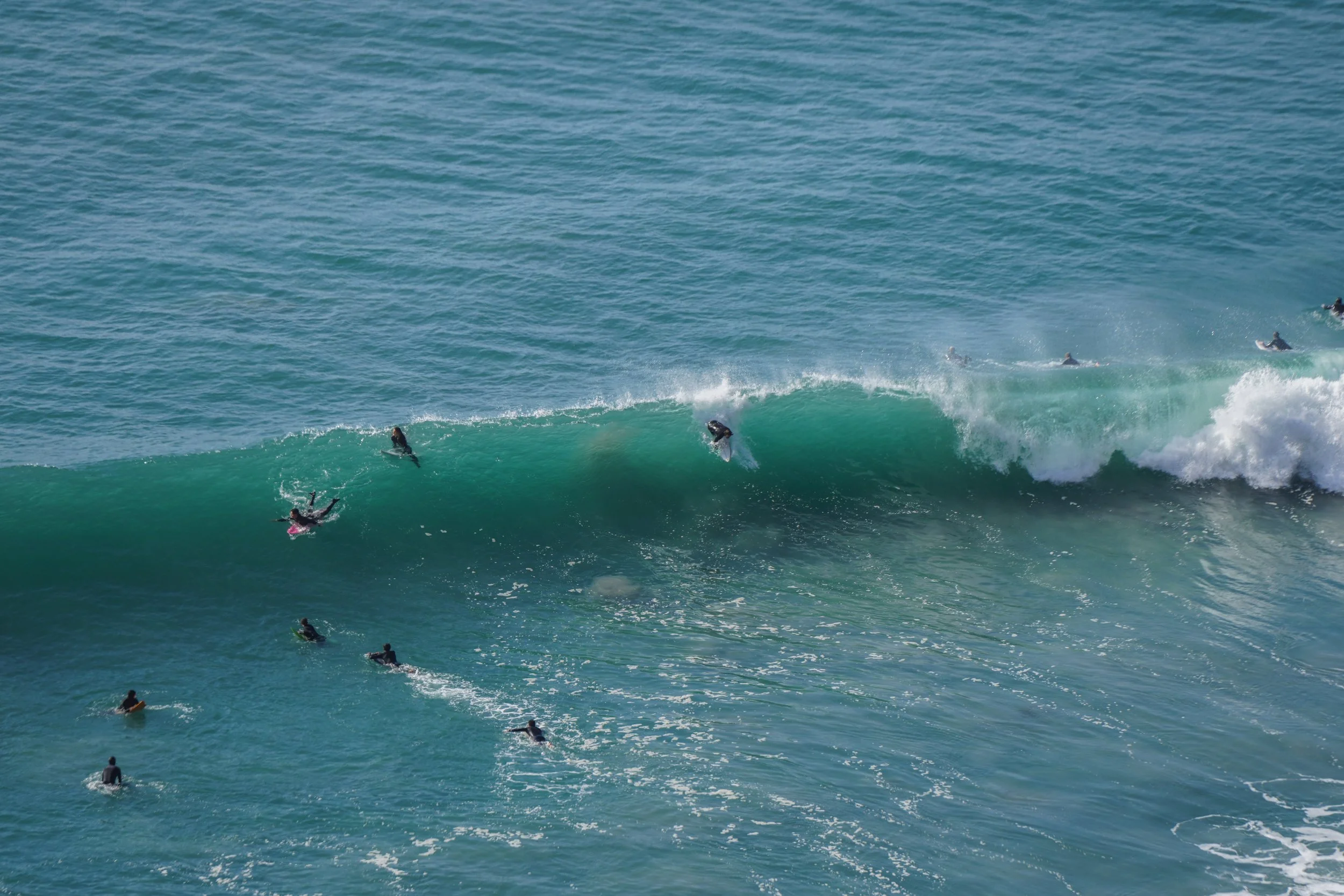 Several surfers riding and waiting for waves in the ocean. Some surfers are on their boards trying to catch a wave while others are paddling in the water.