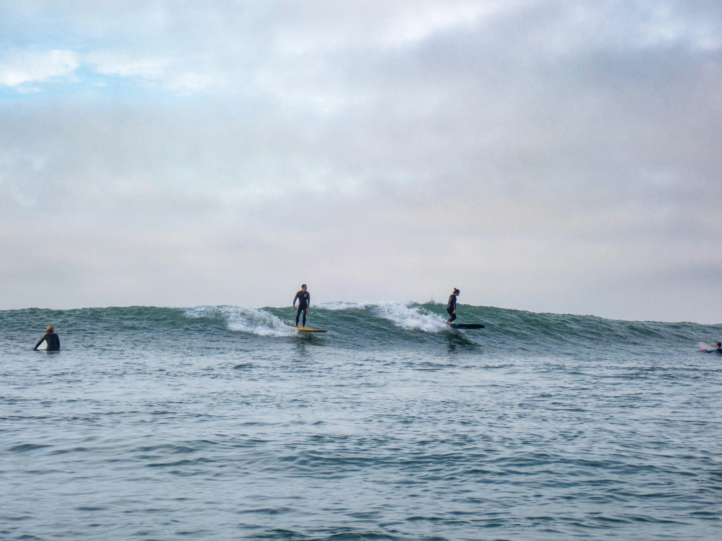 Group of surfers riding small waves in the ocean under cloudy sky.