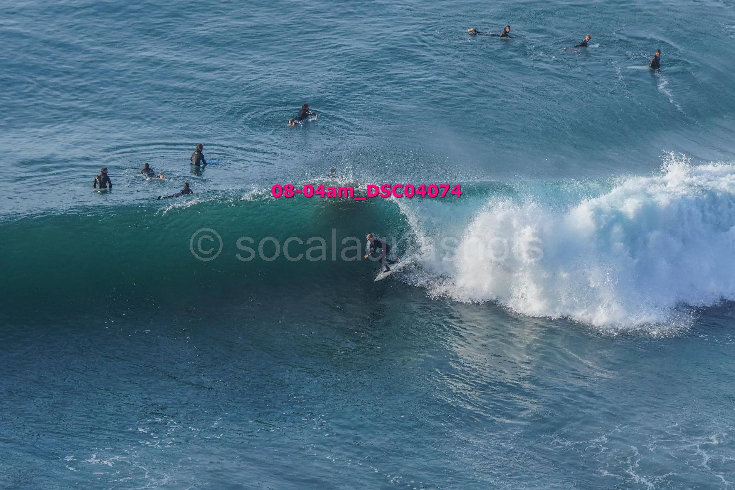 Surfer riding a wave with several people in the water watching from the background.
