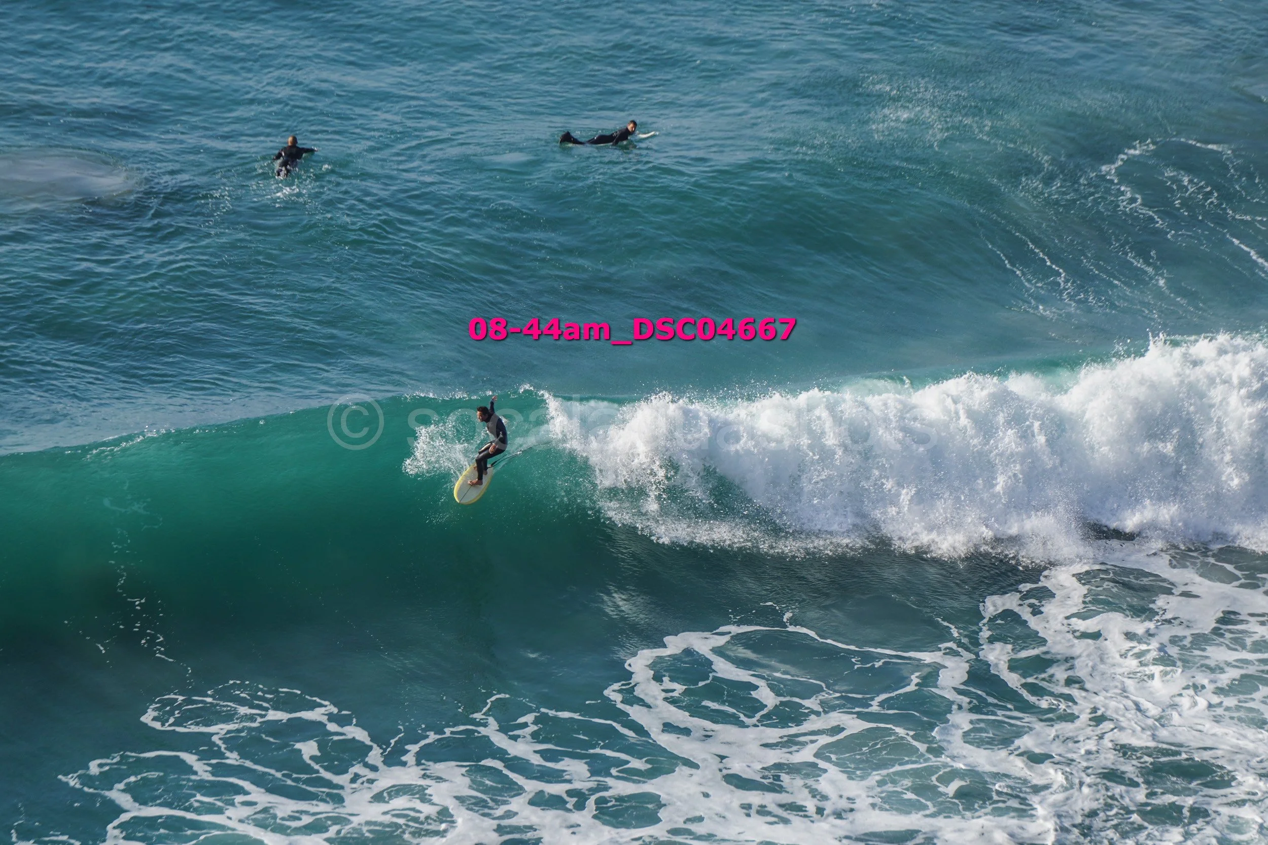 A surfer riding a wave in the ocean with three other surfers nearby.