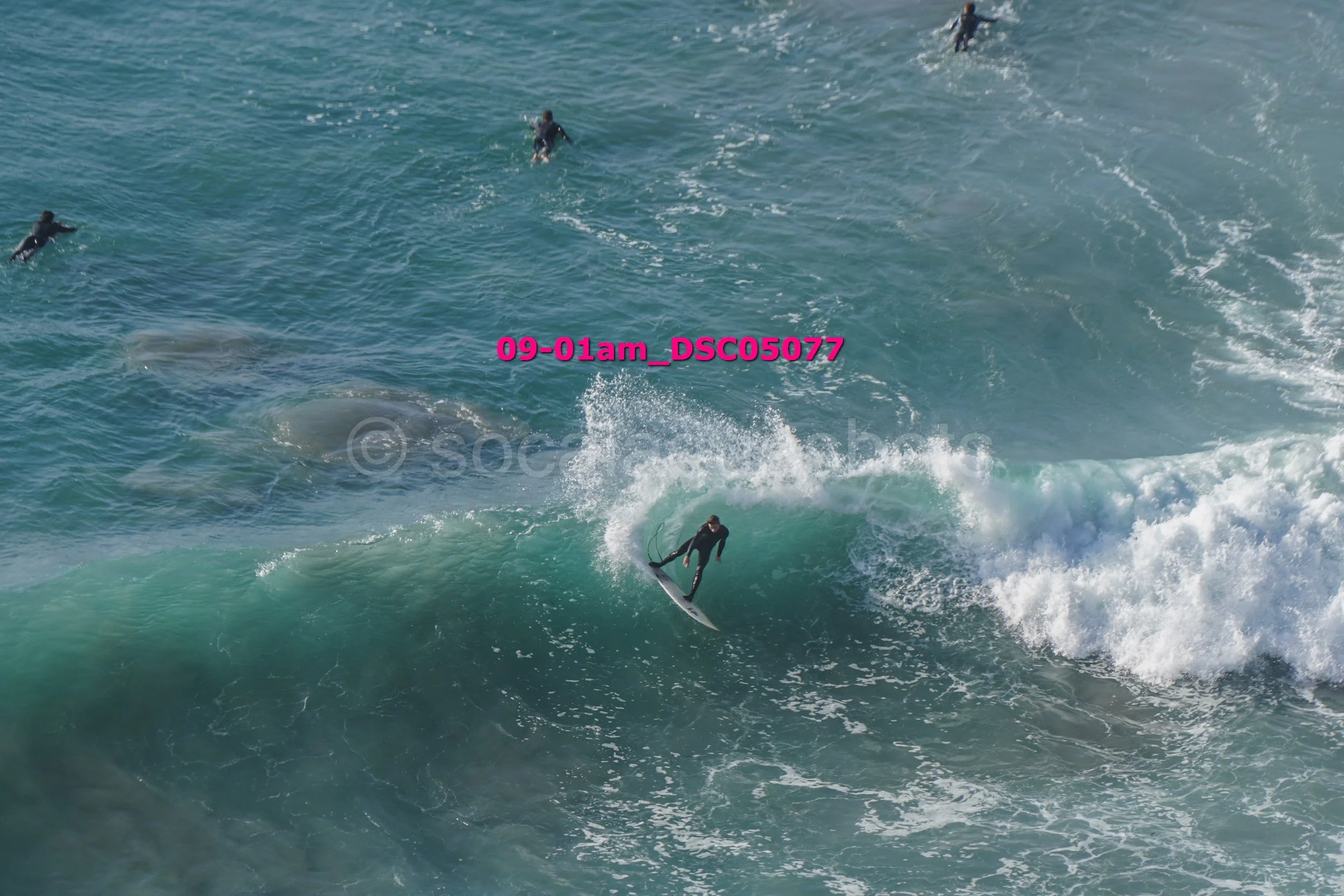 A person surfing on a wave with several other surfers in the water around them.