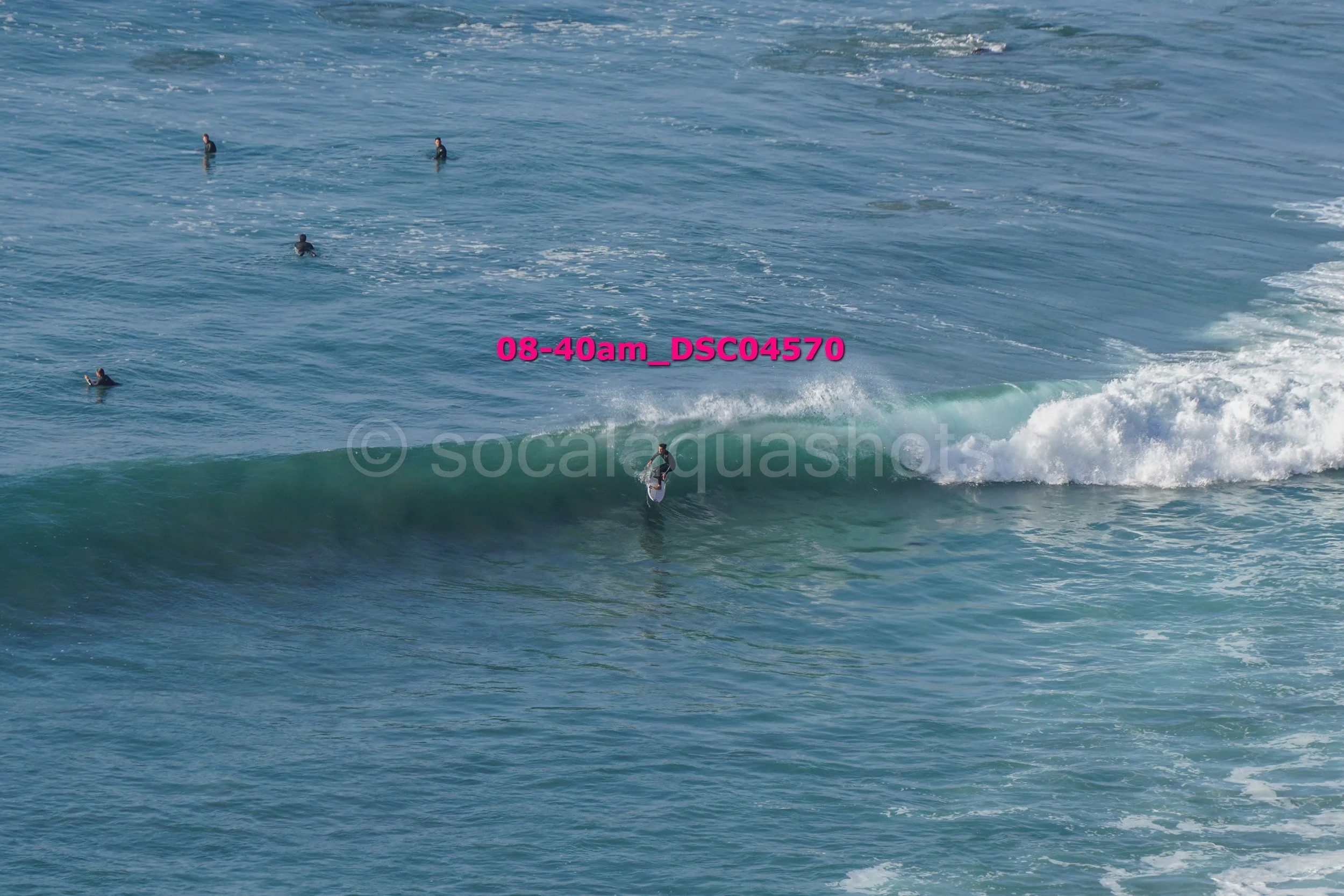 A surfer riding a wave in the ocean while several other surfers float in the water nearby.