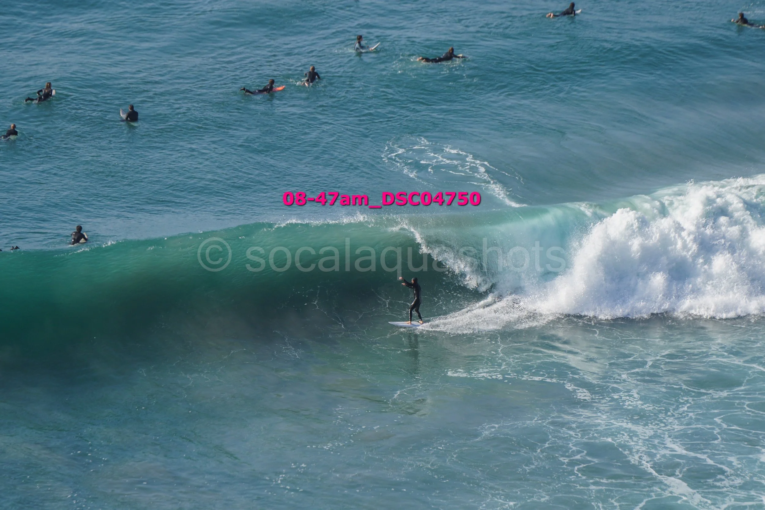 A person surfing on a large wave with multiple surfers in the water watching in the background.