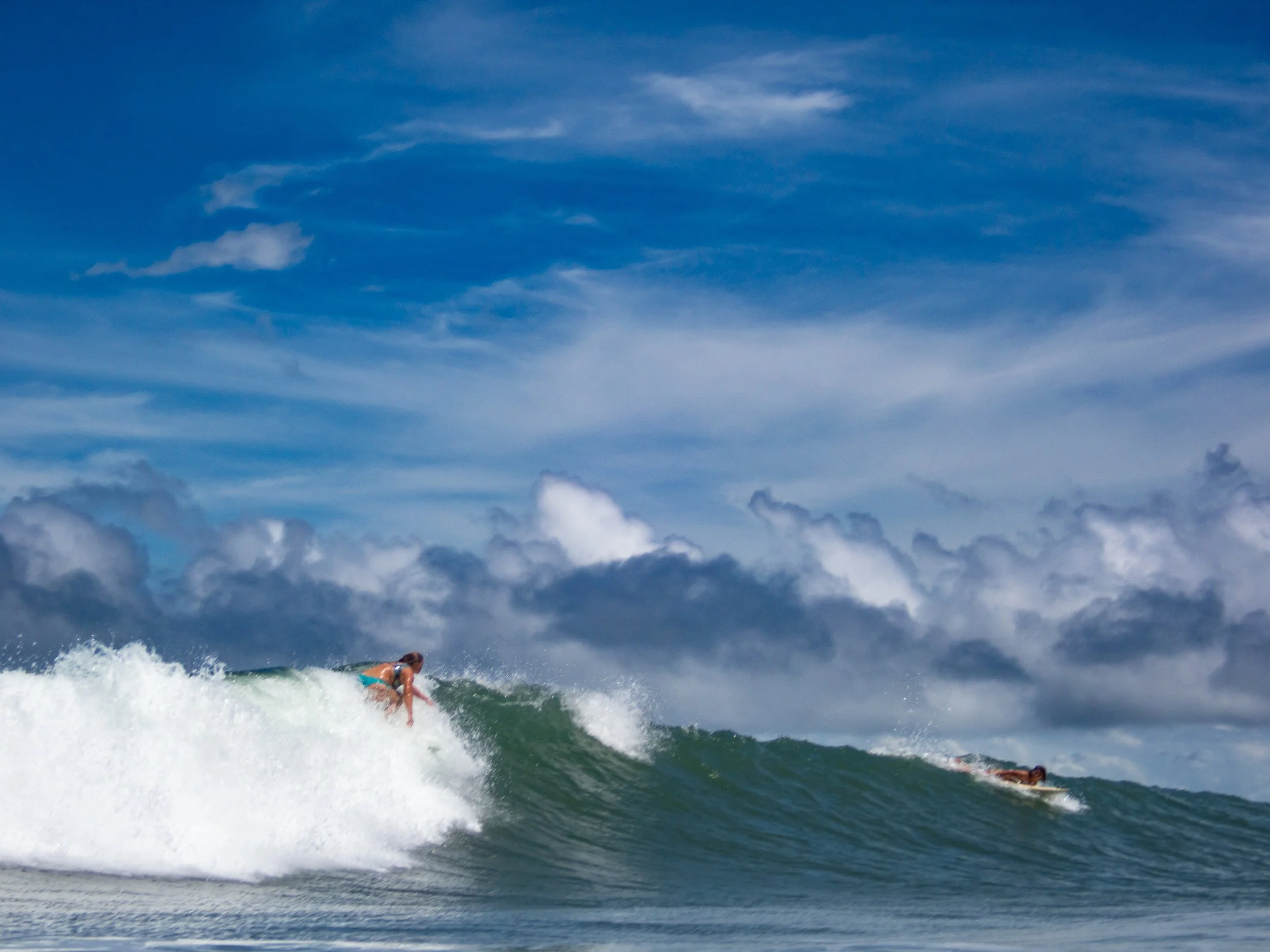 Surfers riding waves under a blue sky with clouds