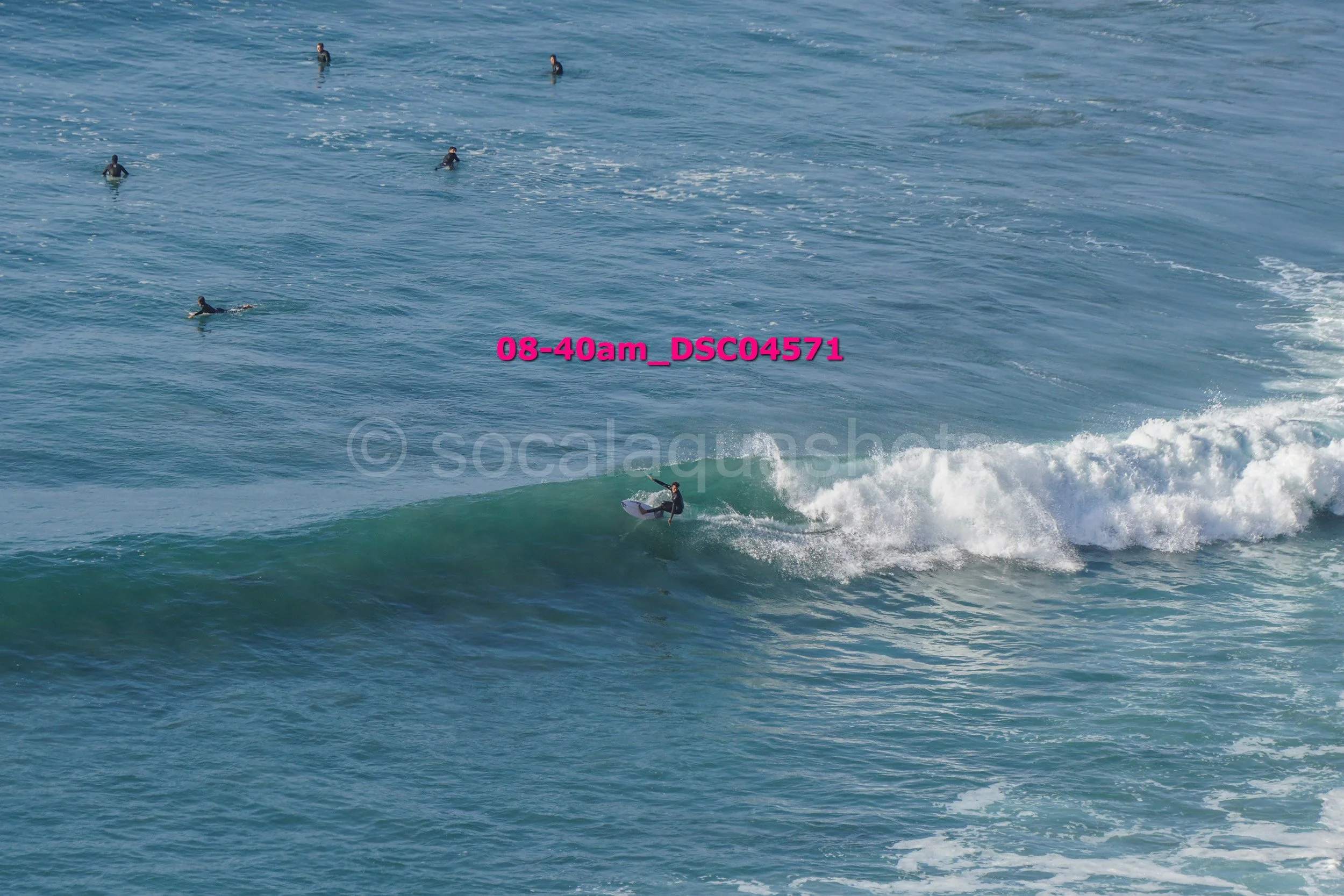 A person surfing on a wave while several other surfers are waiting in the water.