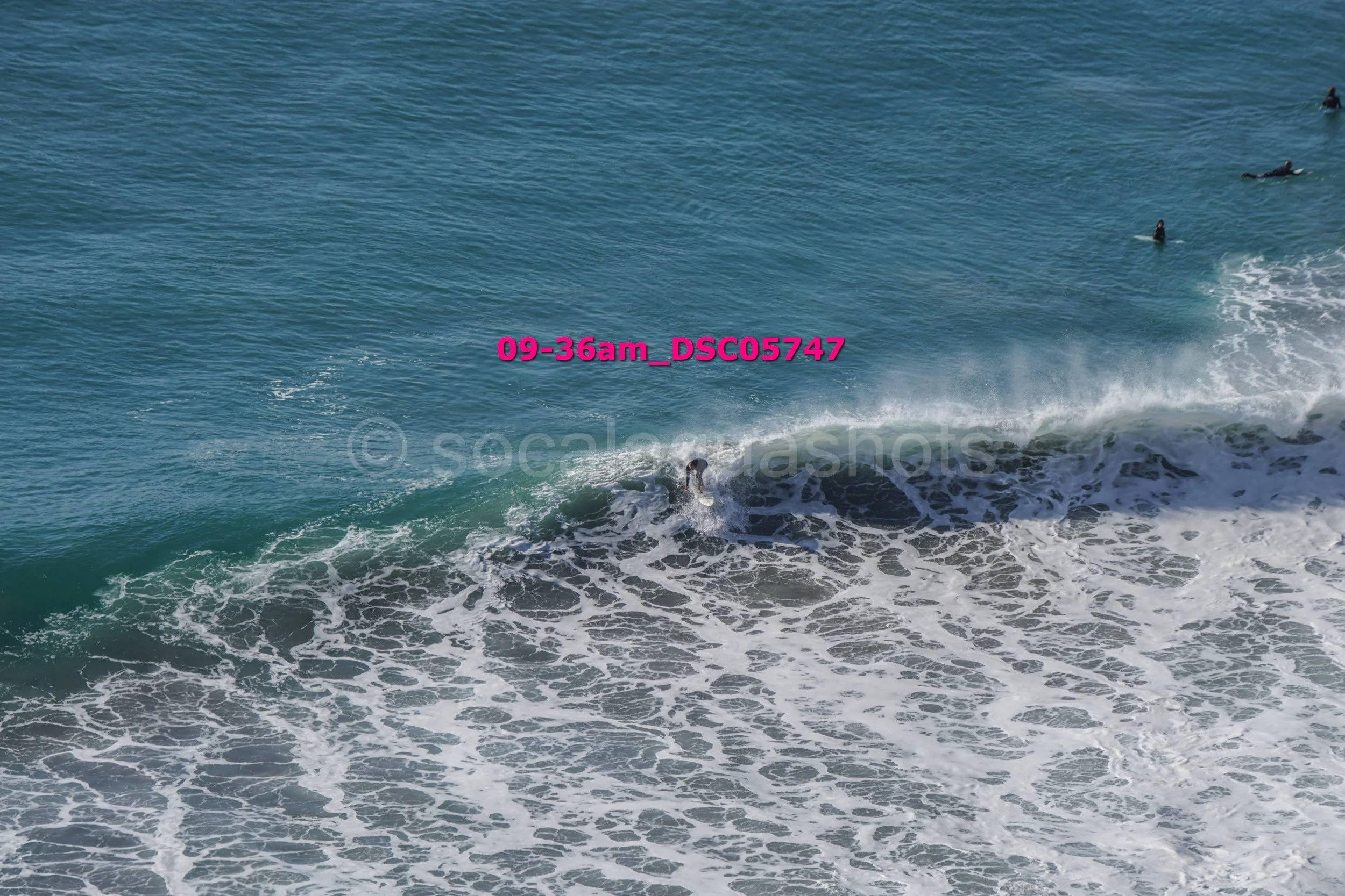 Surfers riding and waiting in the ocean waves near the shore on a clear day.
