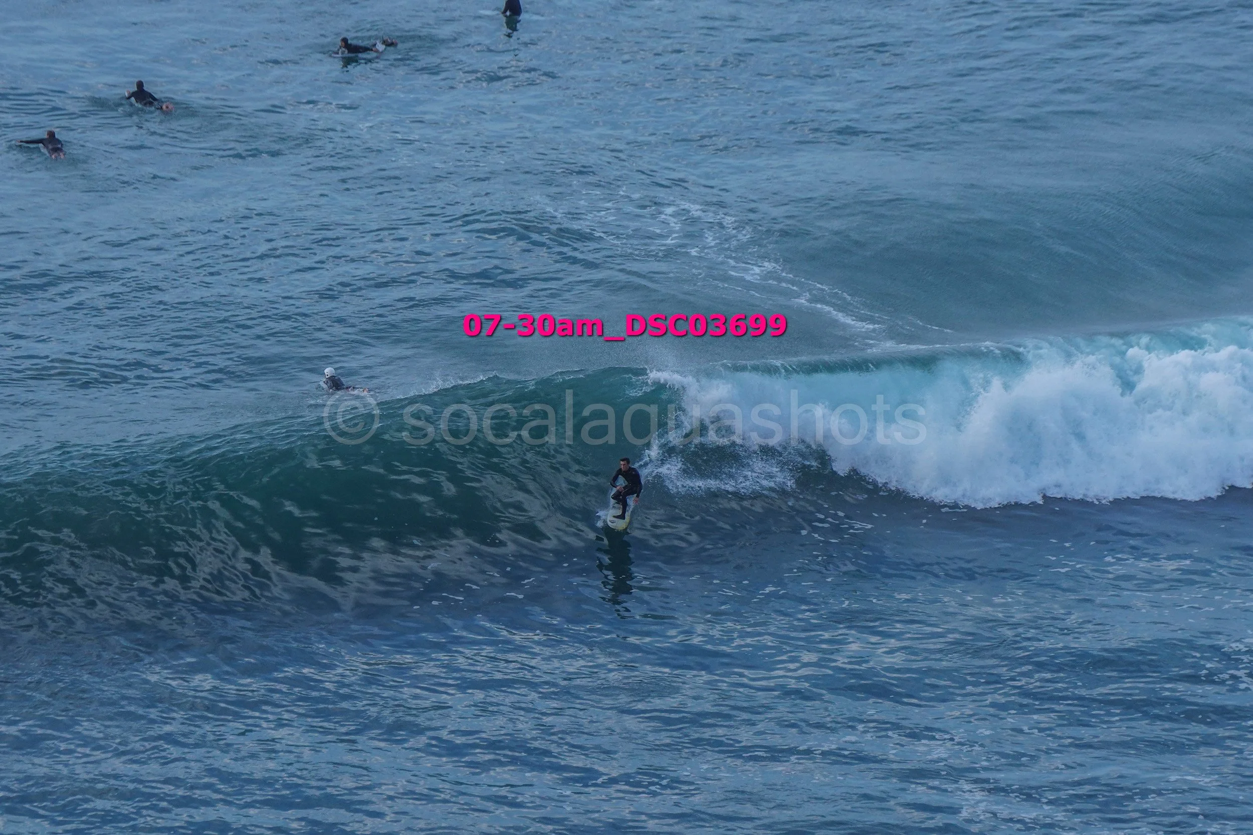 A person surfing on a wave in the ocean with several other surfers in the background.
