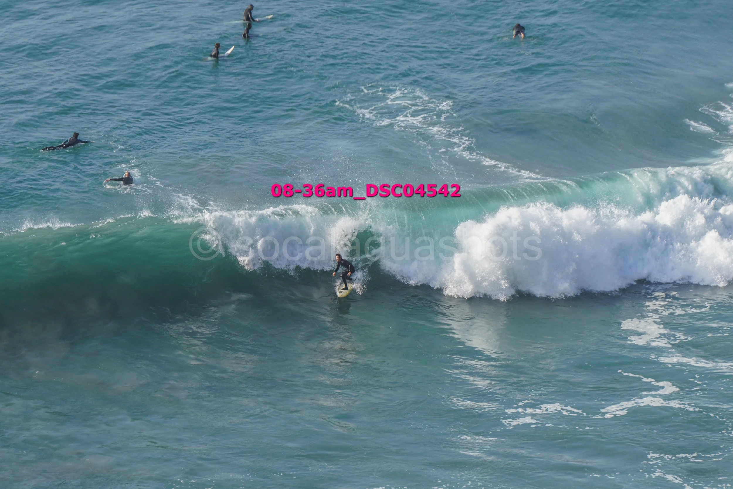 A person surfing on a wave with several other surfers in the water around them.