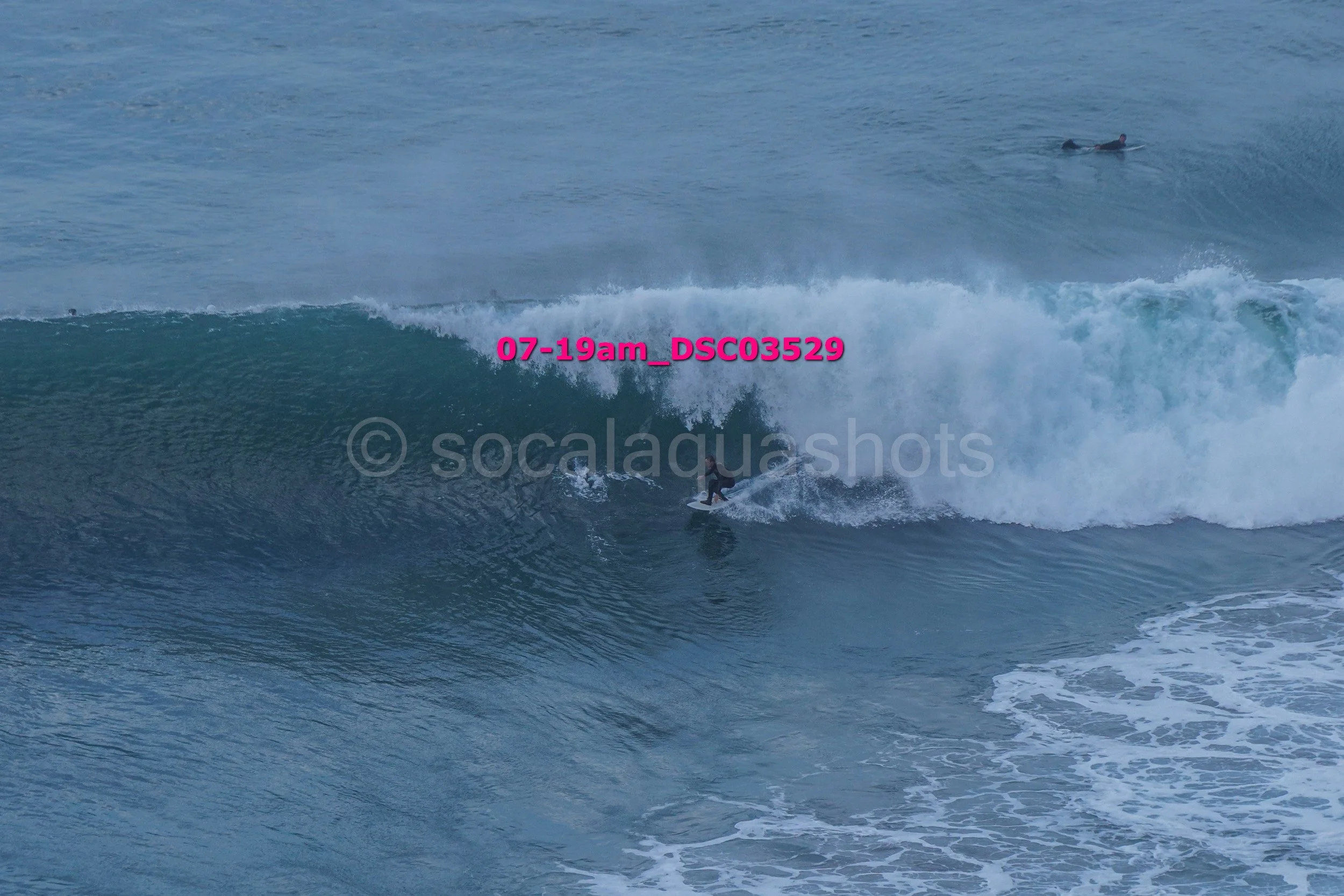 A surfer riding a large wave in the ocean with a person in the water on a surfboard in the background.