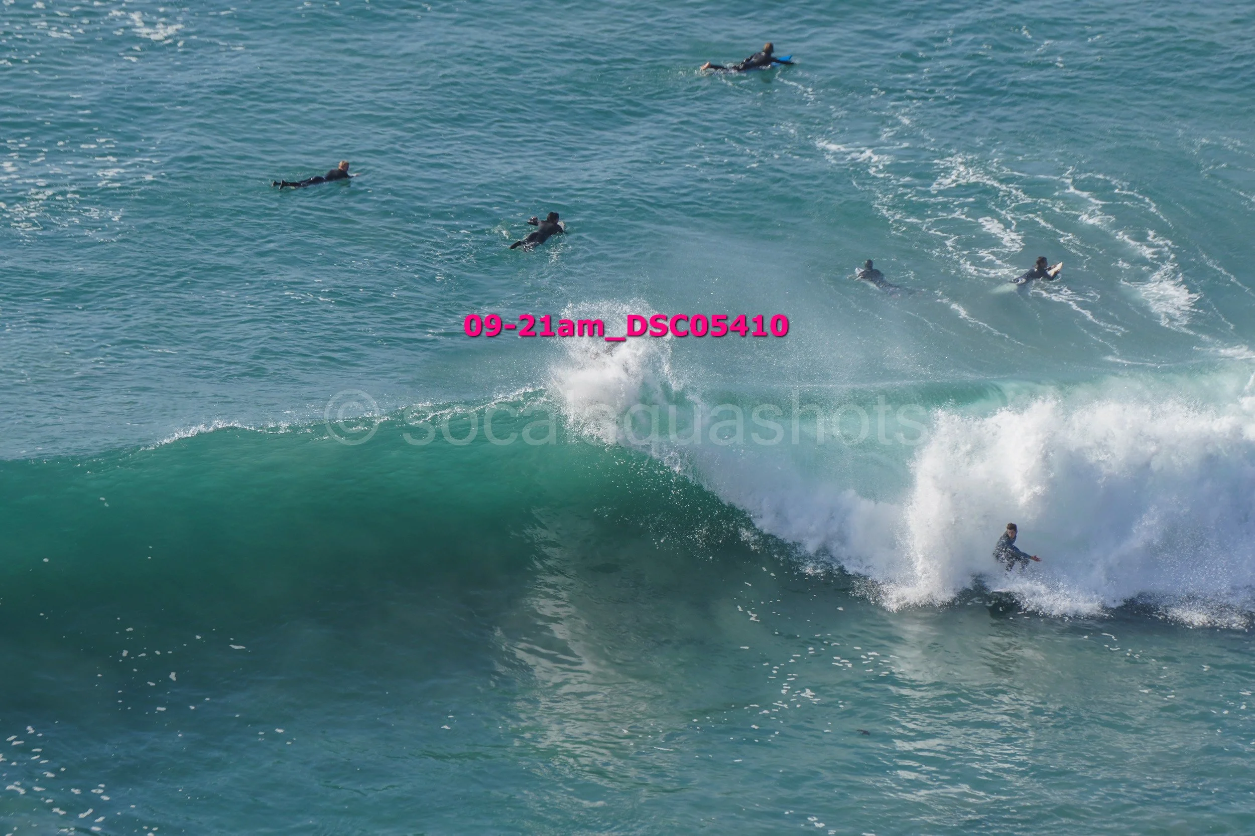 Surfer riding a large wave with multiple surfers in the water nearby.