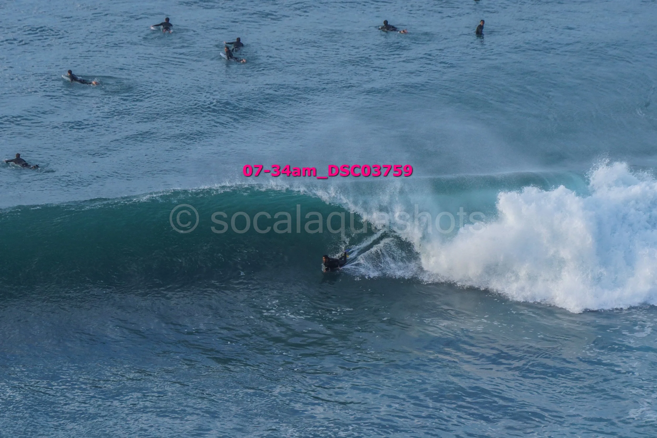 Surfer riding a wave with several other surfers in the background in the ocean.