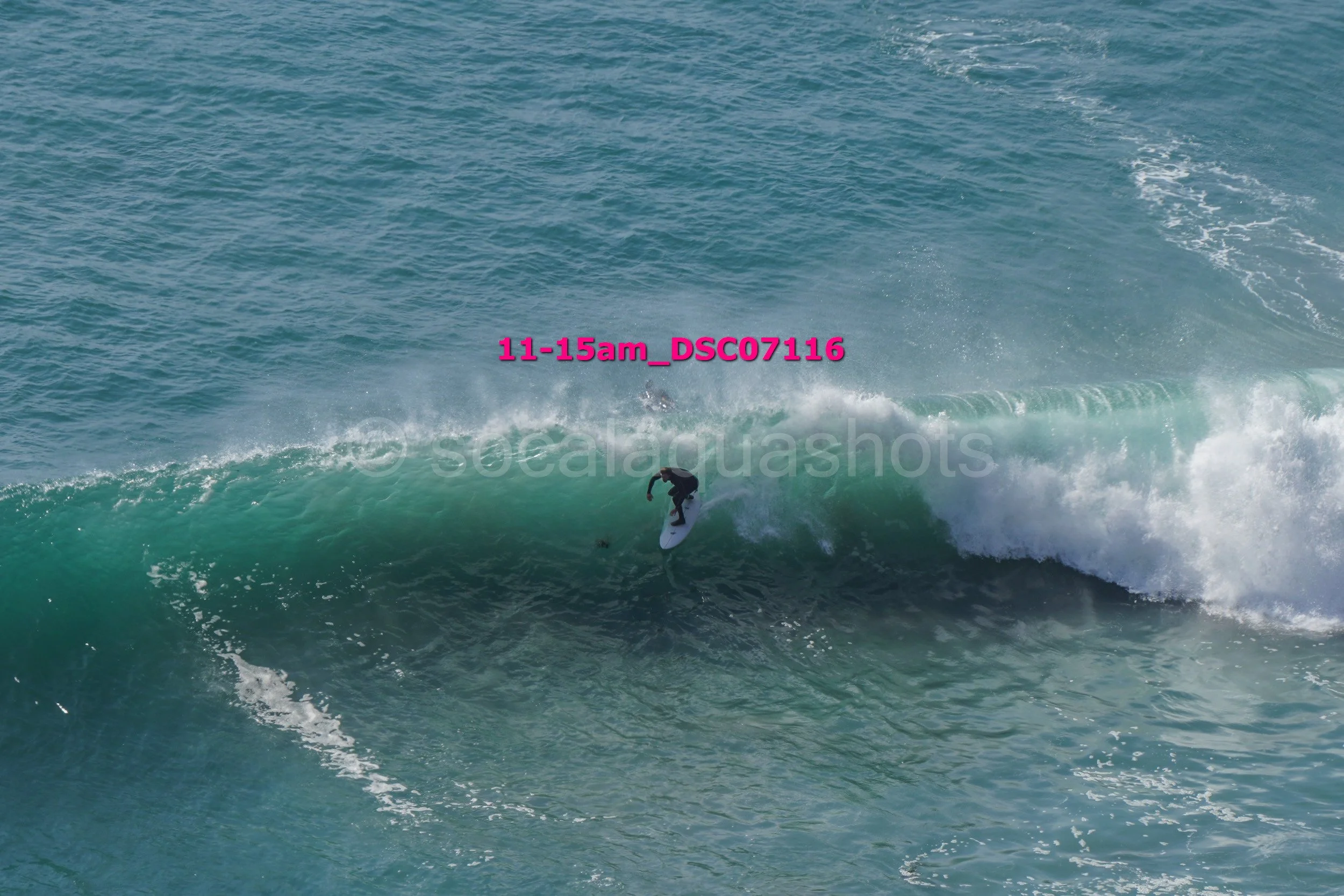 A person surfing on a large wave in the ocean, with the text '11-15am_DSC07116' overlayed in pink.