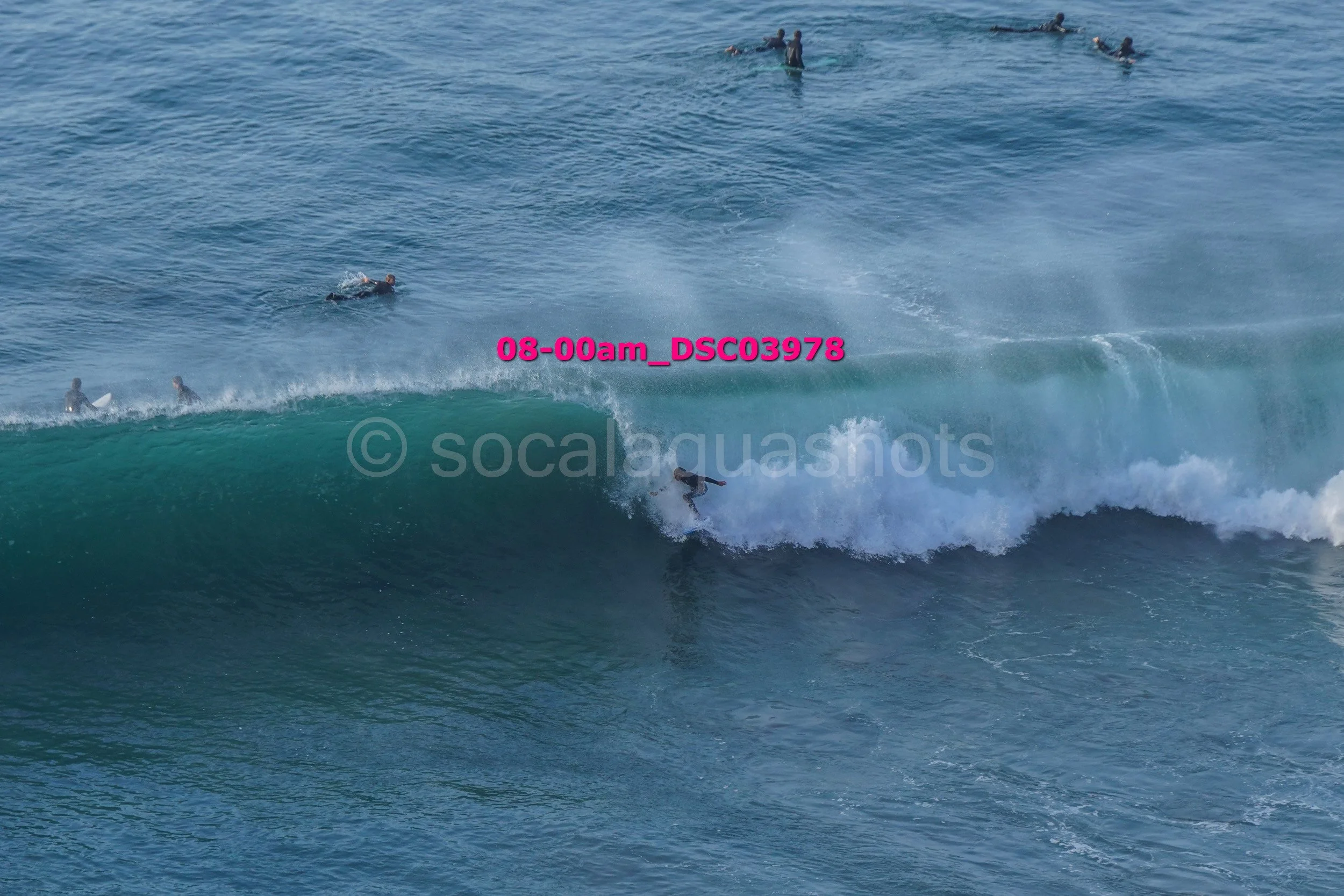 Surfer riding a wave in the ocean with several other surfers in the background.