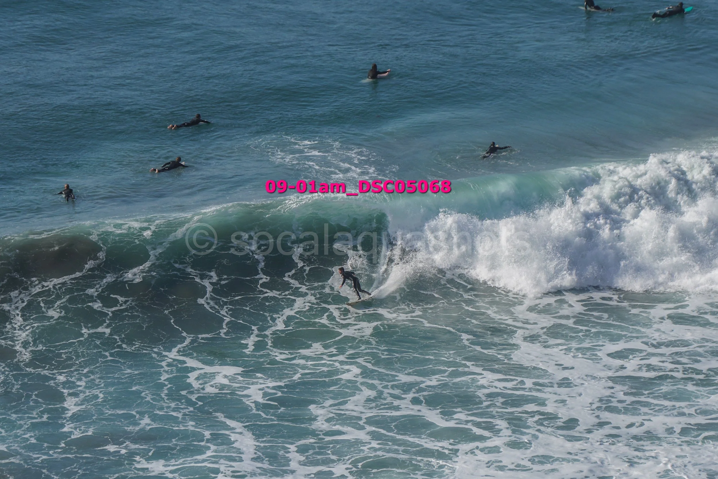 A person surfing on a wave while other surfers wait in the water nearby.