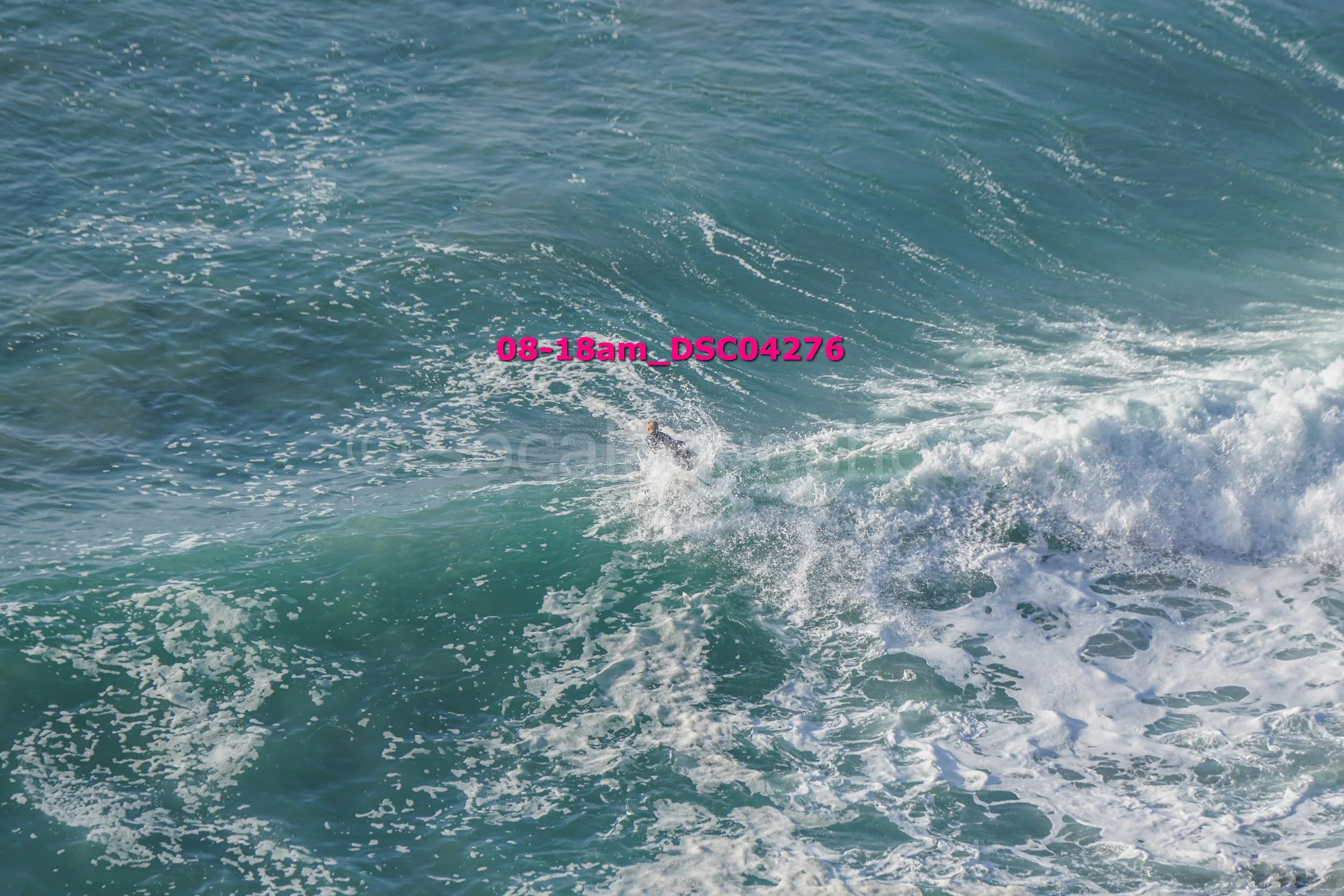 Sea waves with a surfer riding on a wave, sunset lighting, sending spray into the air, timestamp and file name text overlay.