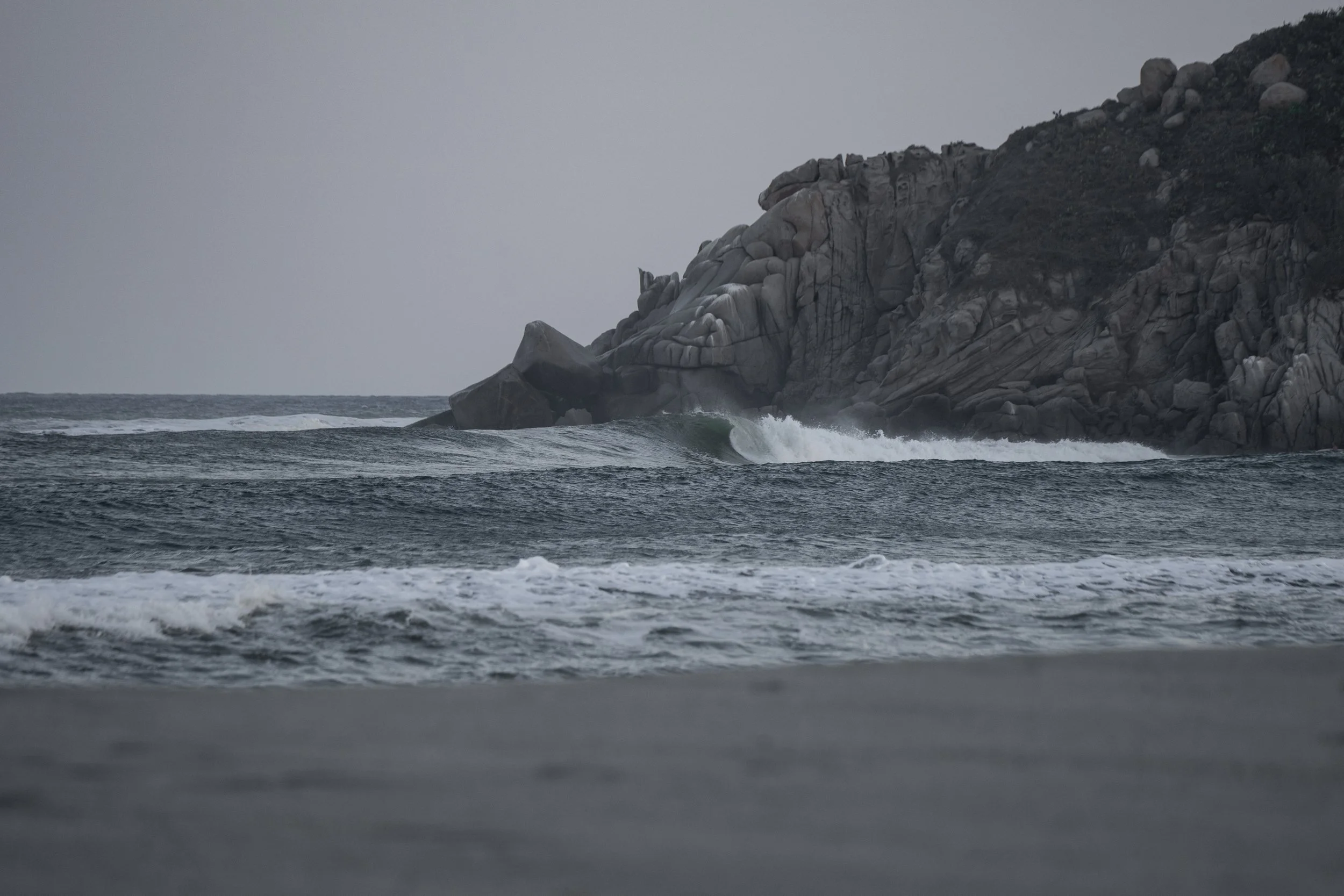 Overcast sky over ocean with waves and rocky coast on the right.