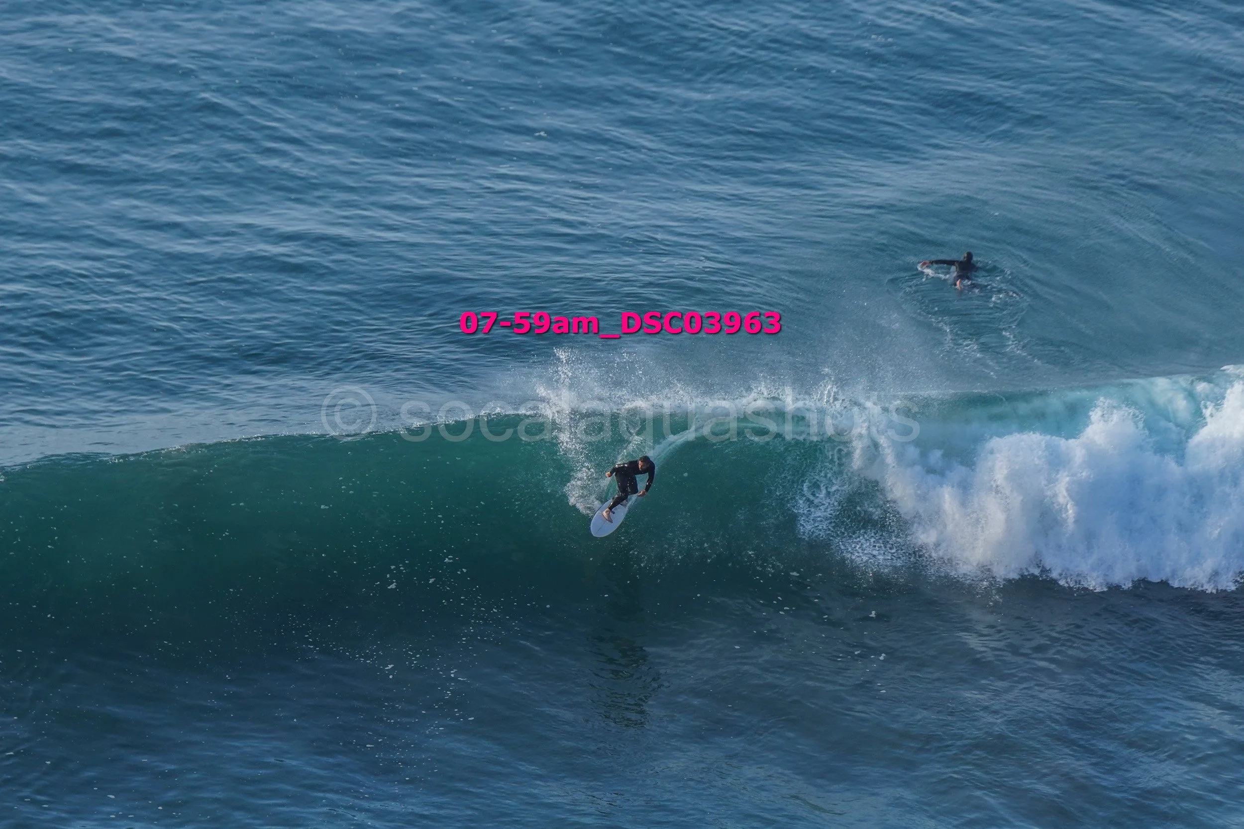 A surfer riding a wave with another person swimming in the ocean nearby.