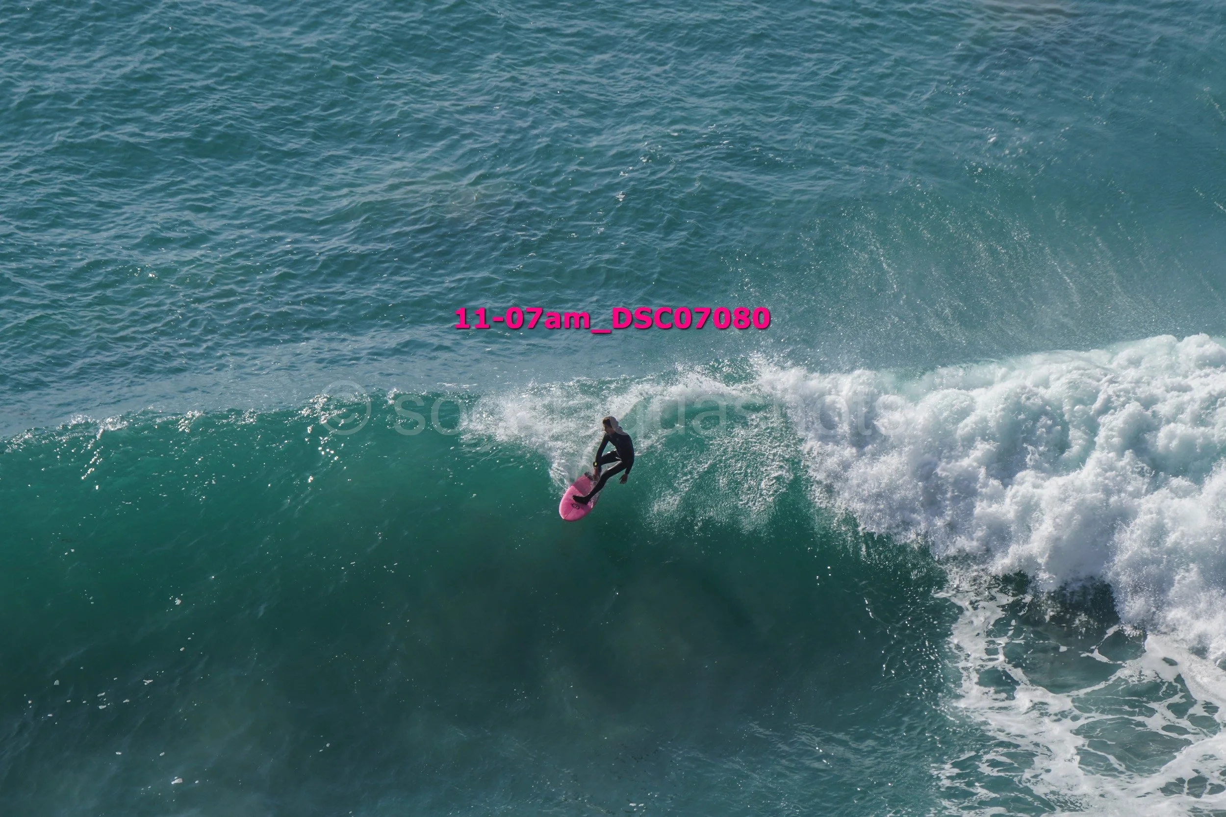 A person surfing on a pink surfboard riding a wave in the ocean.